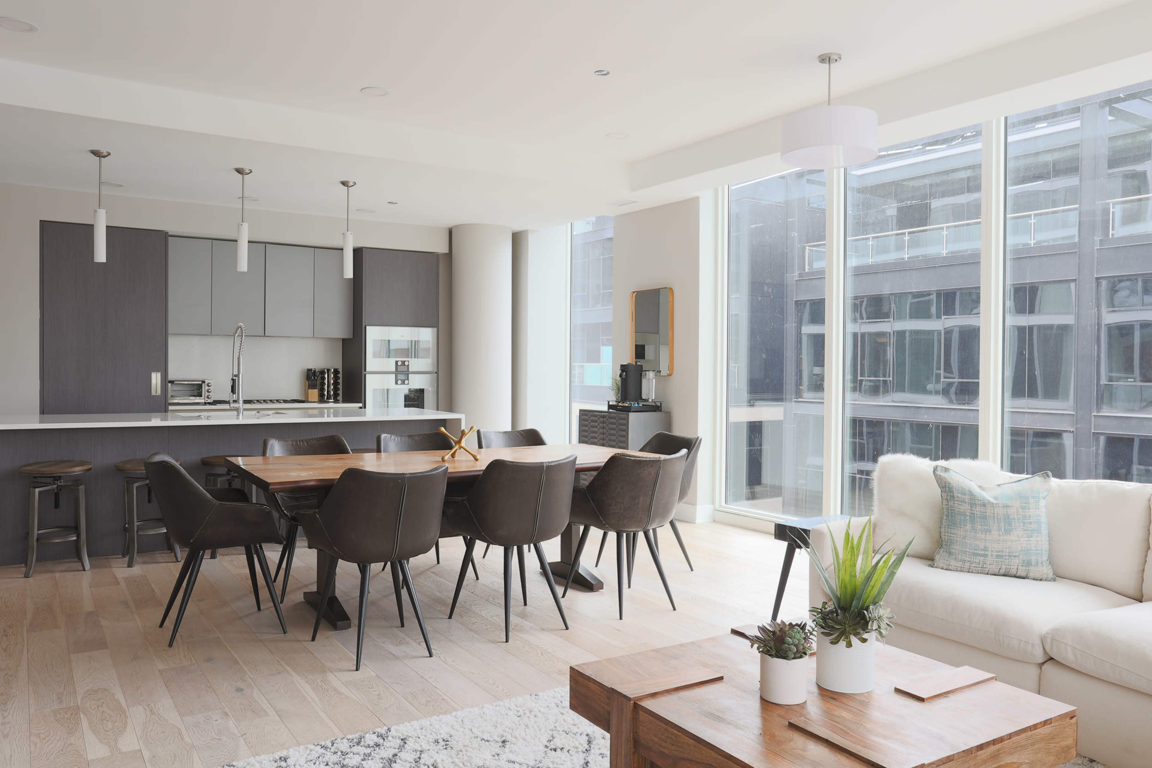 A modern open-plan living and dining area features a large table with chairs, a couch, and a kitchen with sleek cabinetry.