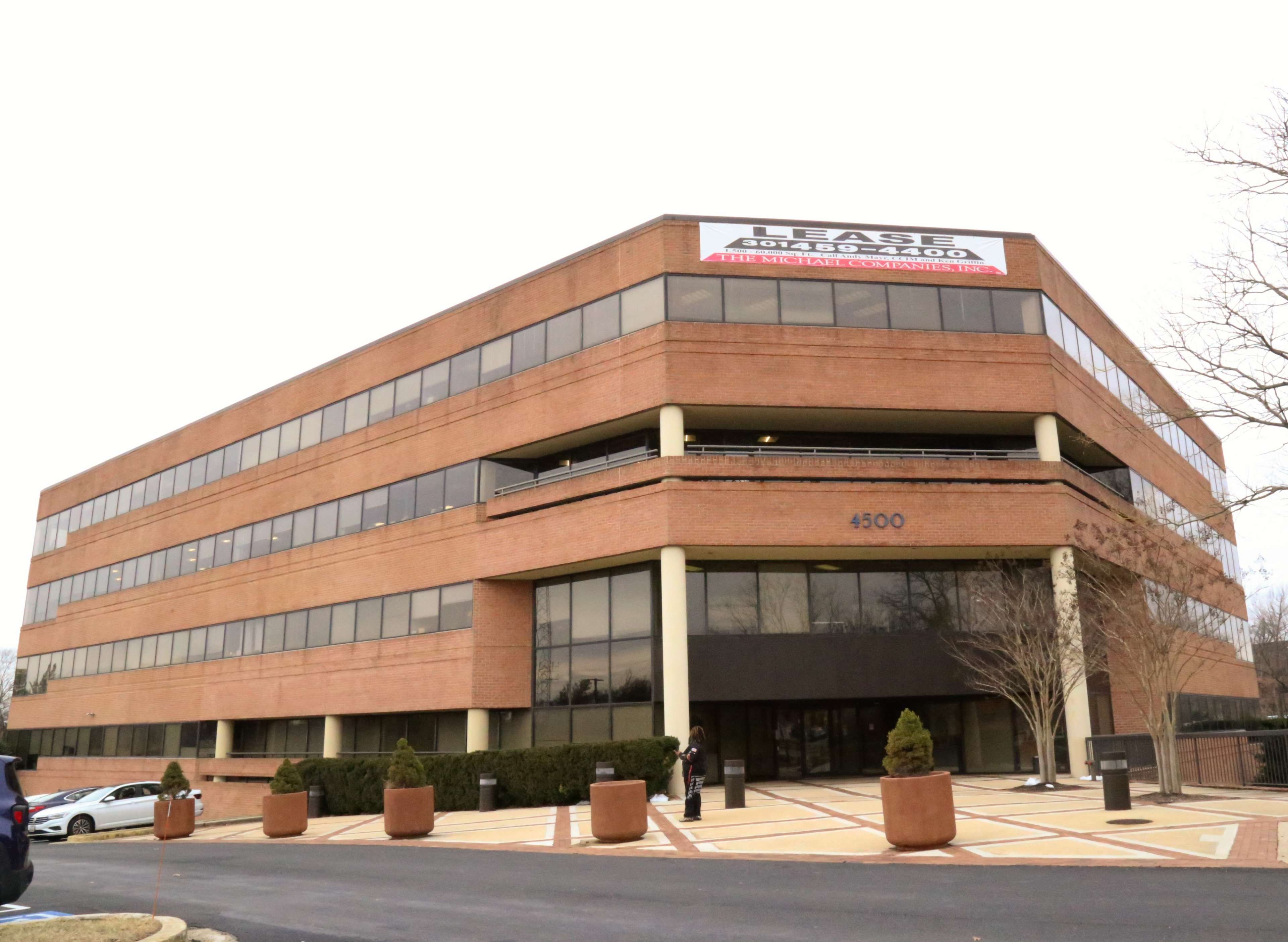 A modern, multi-story office building with a for-lease sign prominently displayed at the top.