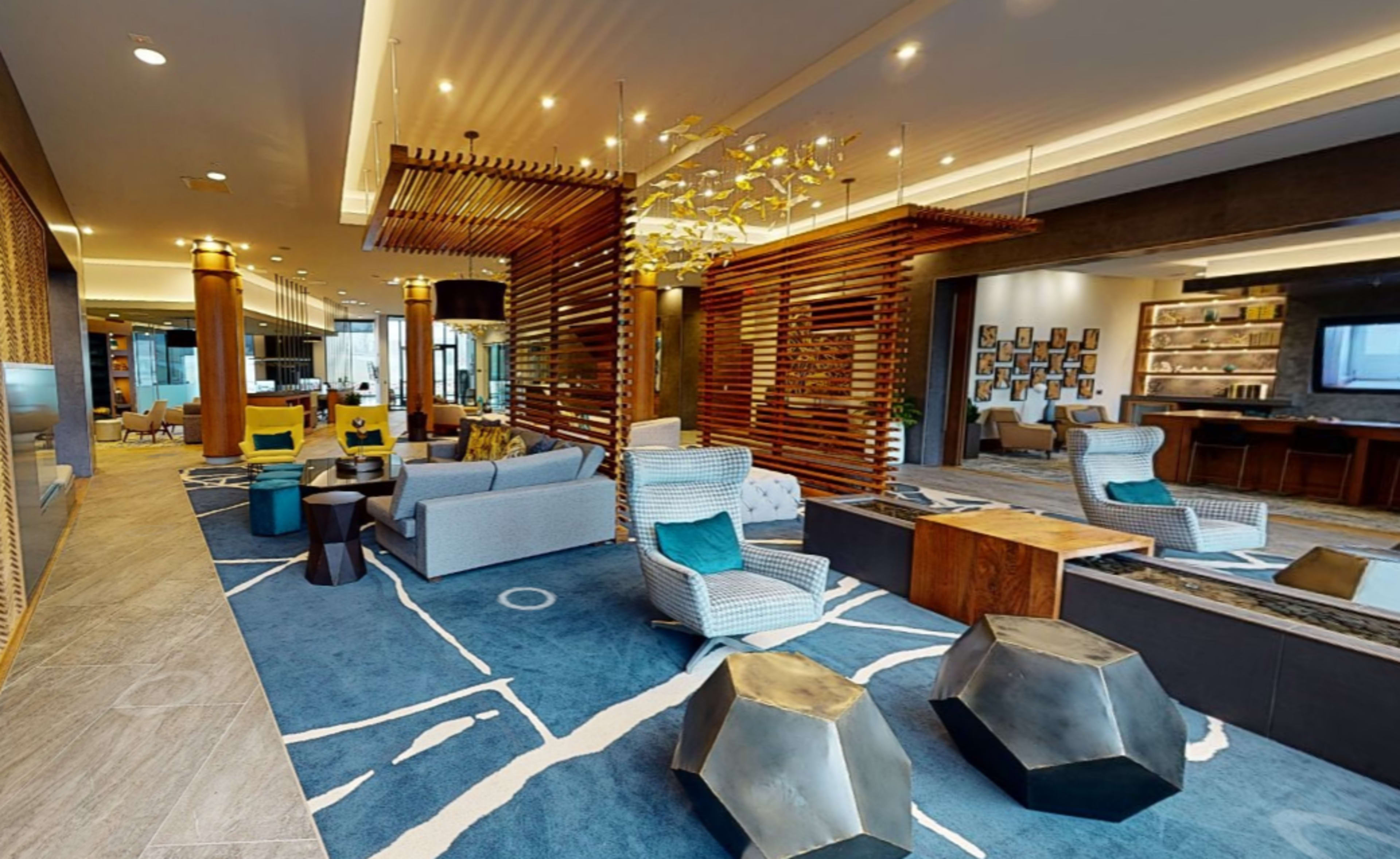 A modern lobby with seating areas, wooden dividers, and a large area rug featuring abstract patterns.