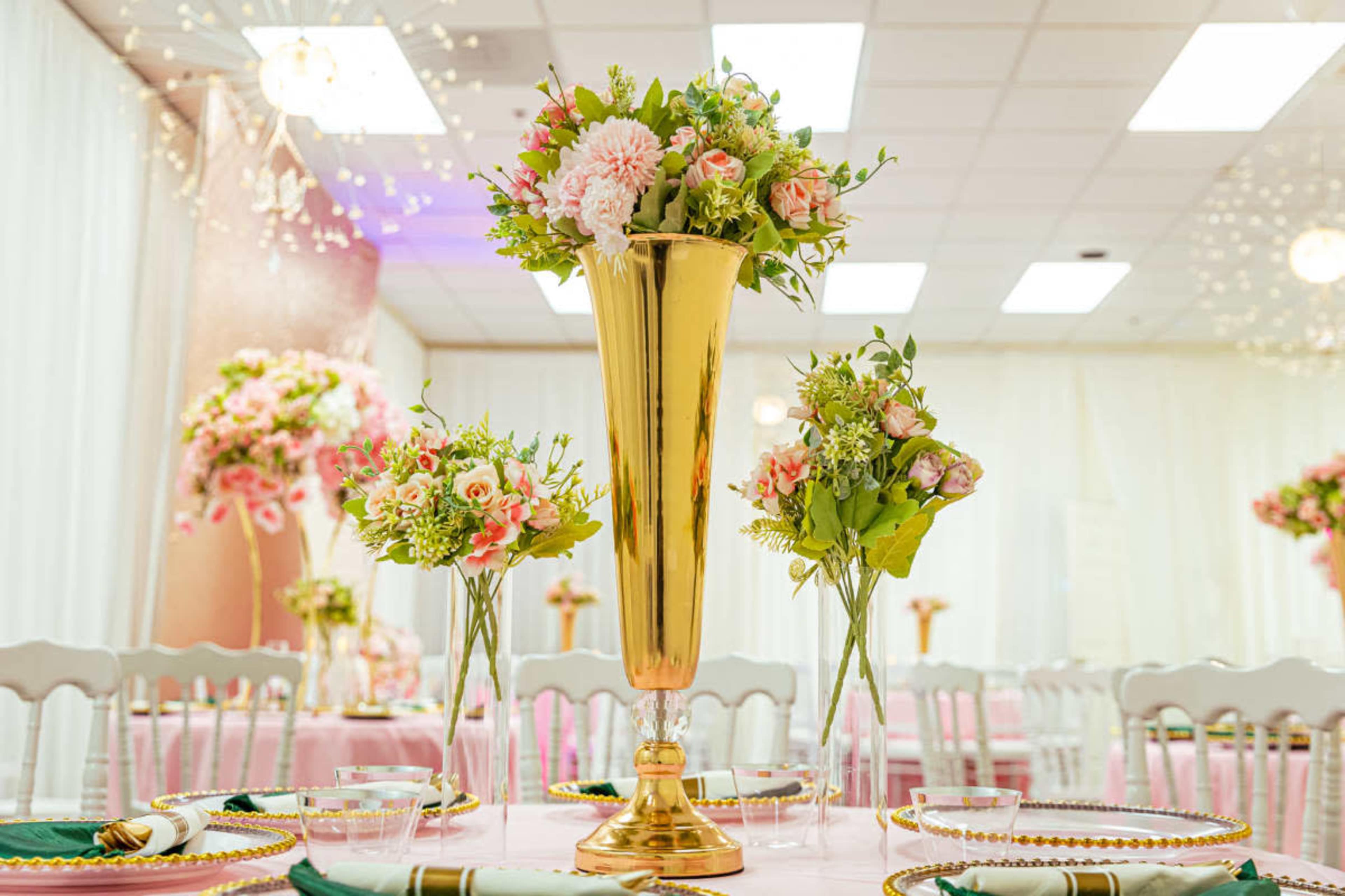 A banquet setup featuring tall golden vases filled with floral arrangements on elegantly set tables.