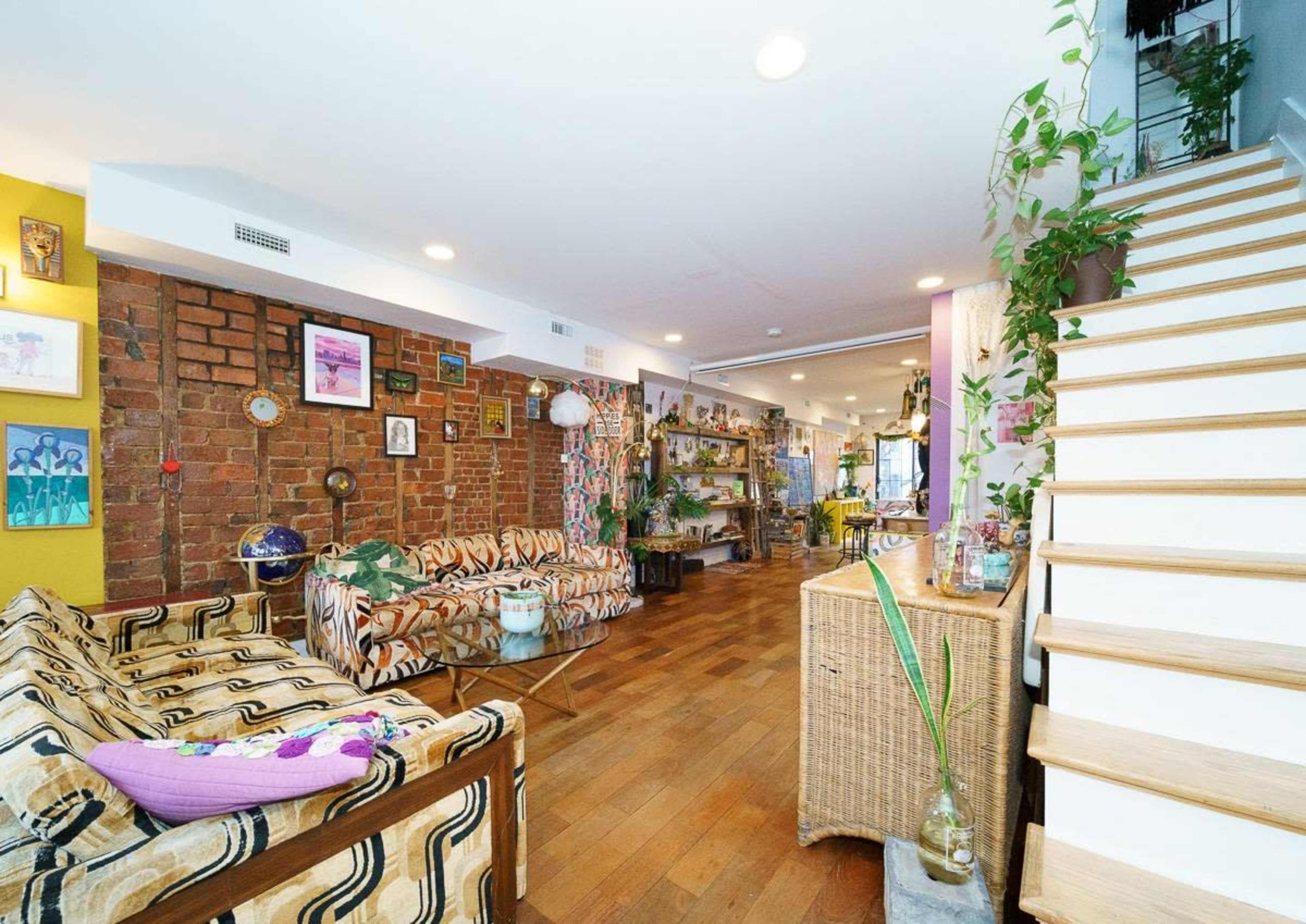 A spacious living area features patterned sofas, exposed brick walls, and wooden floors, with a staircase leading to an upper level.