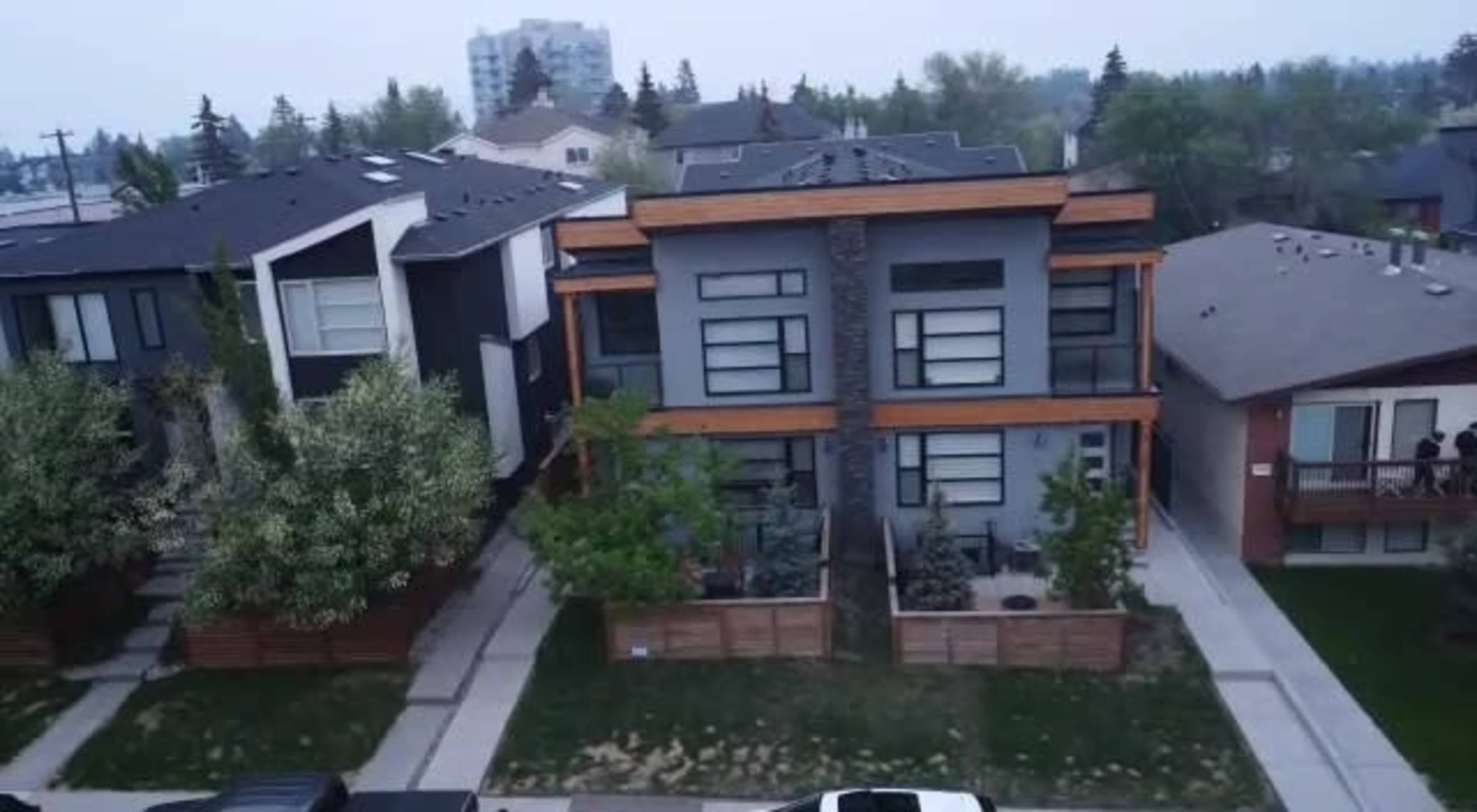 The image shows a row of modern multi-family homes with a mix of dark and light-colored facades, separated by sidewalks and small yards.