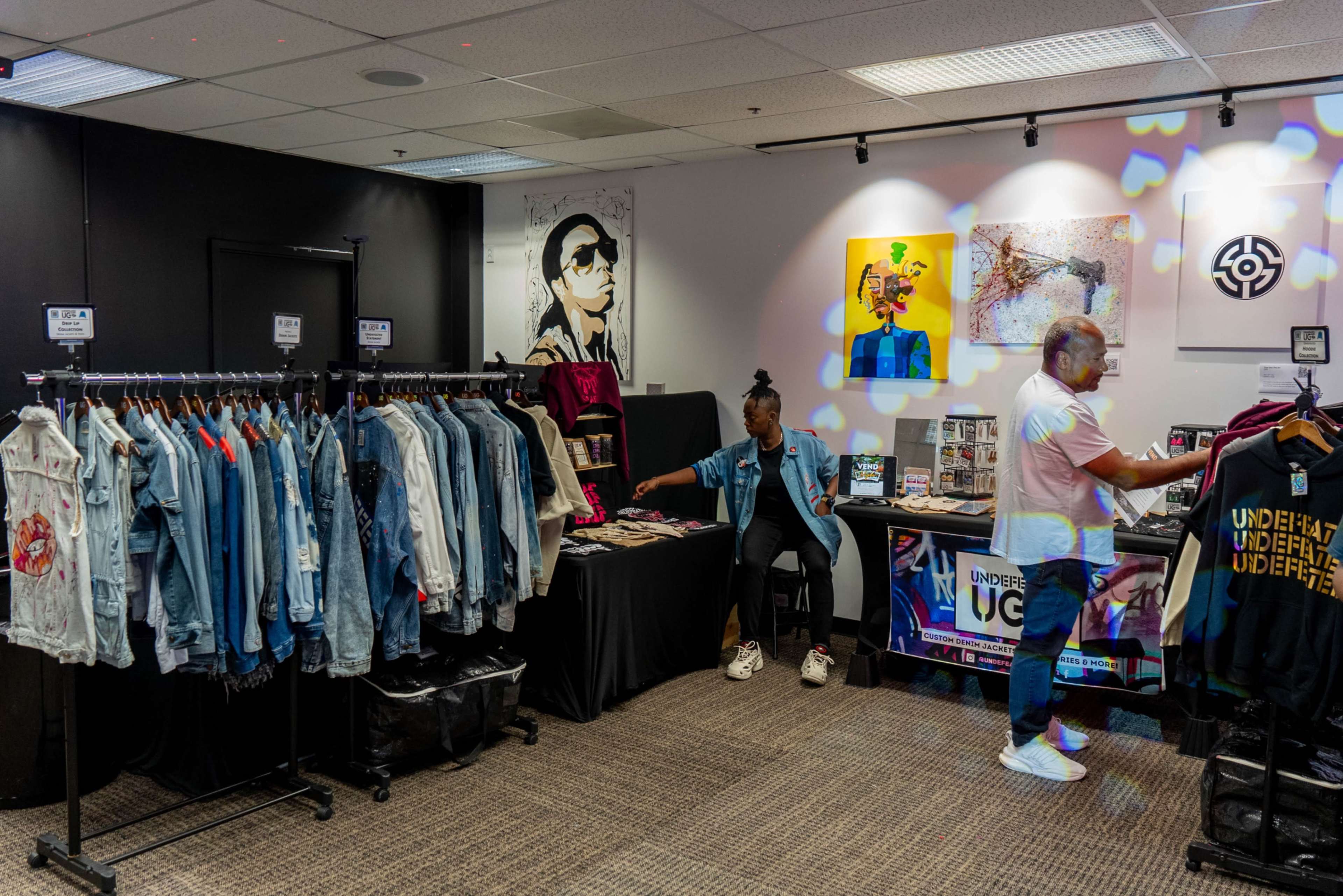The image shows a retail space featuring racks of denim jackets and a display of various merchandise, with a person seated and another attending to a table.