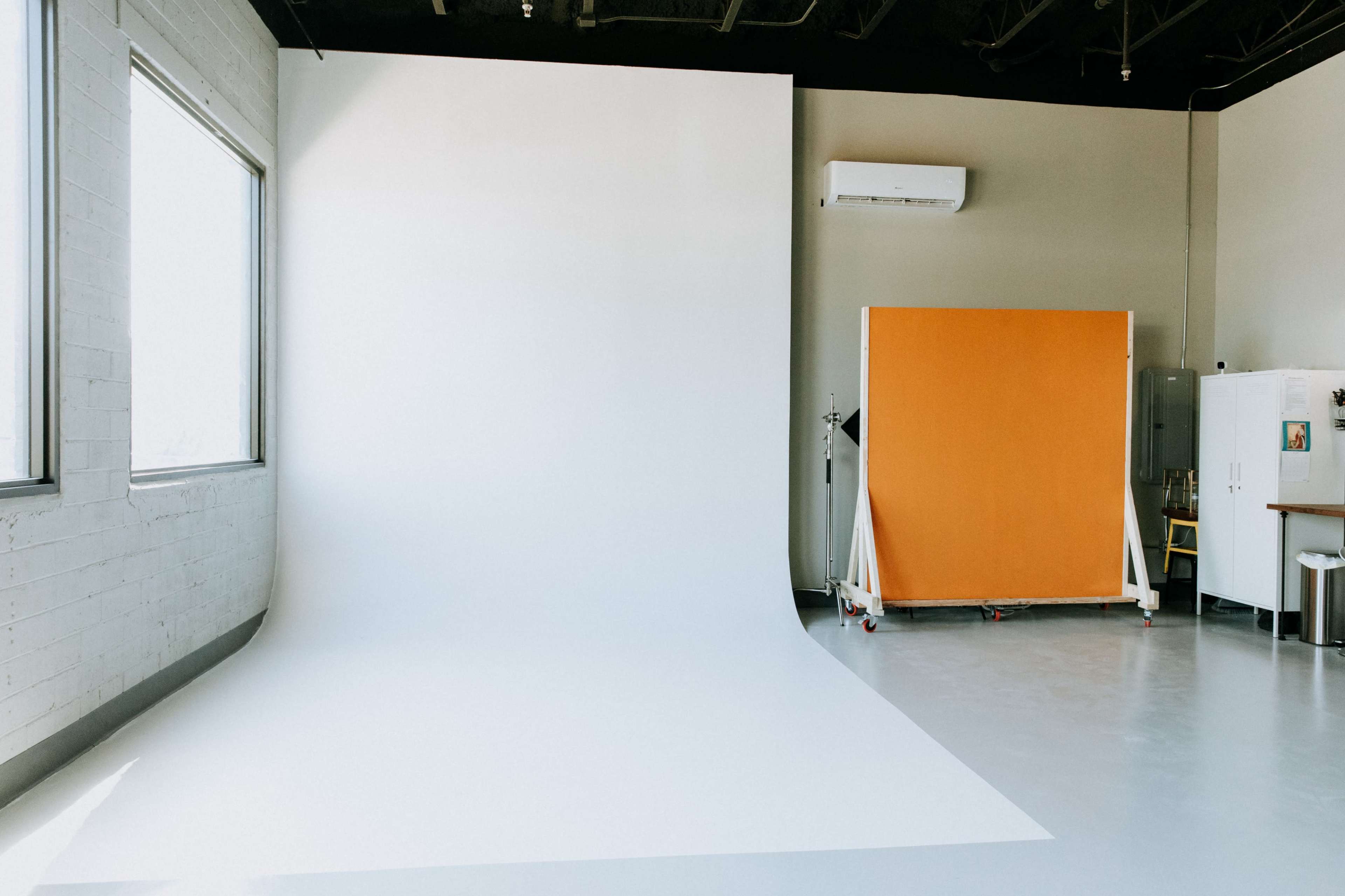 An empty photography studio features a large white backdrop along one wall and an orange partition nearby.