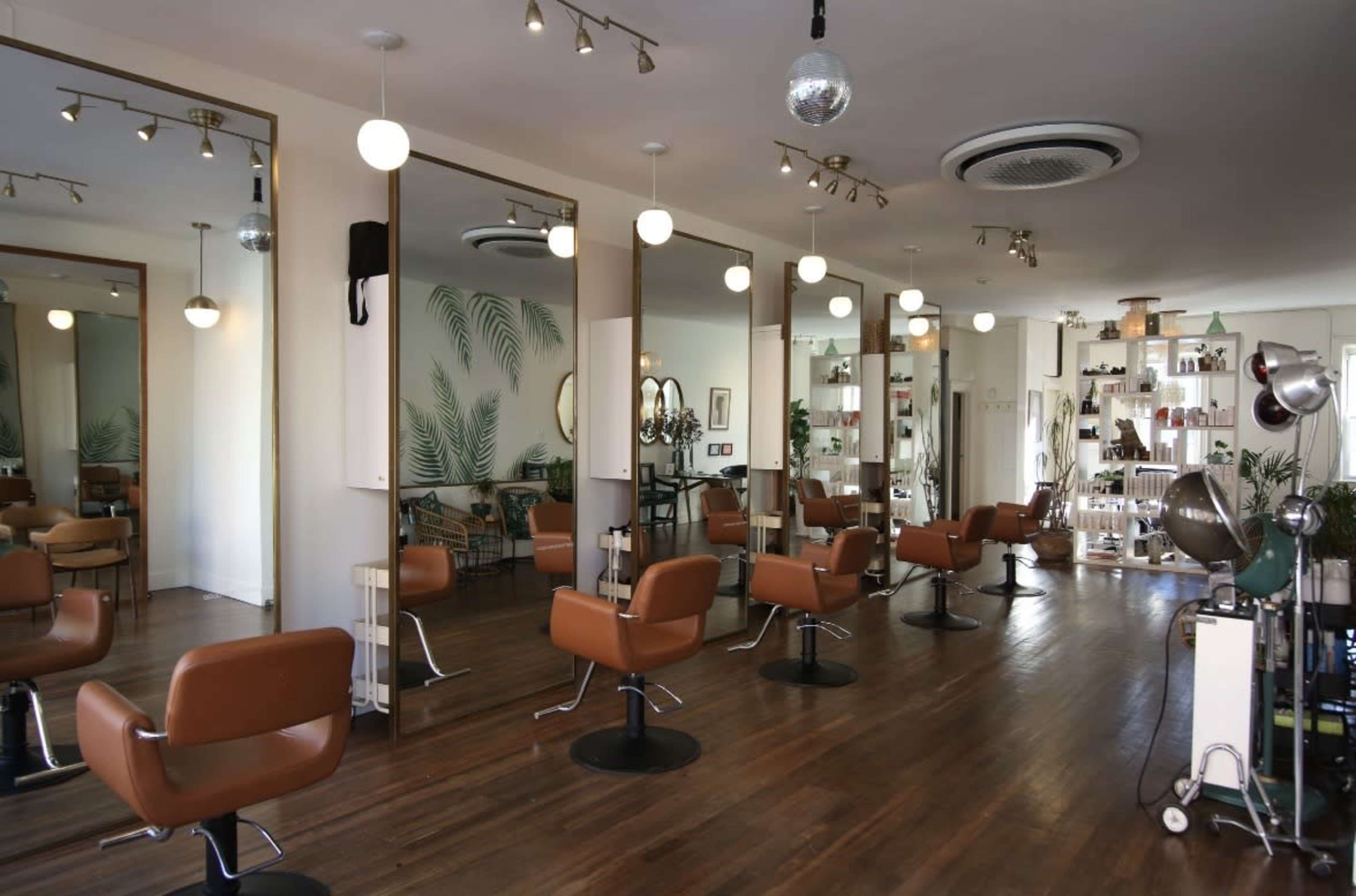 The image shows a modern hair salon with brown styling chairs, large mirrors, and a well-organized display of hair products in the background.