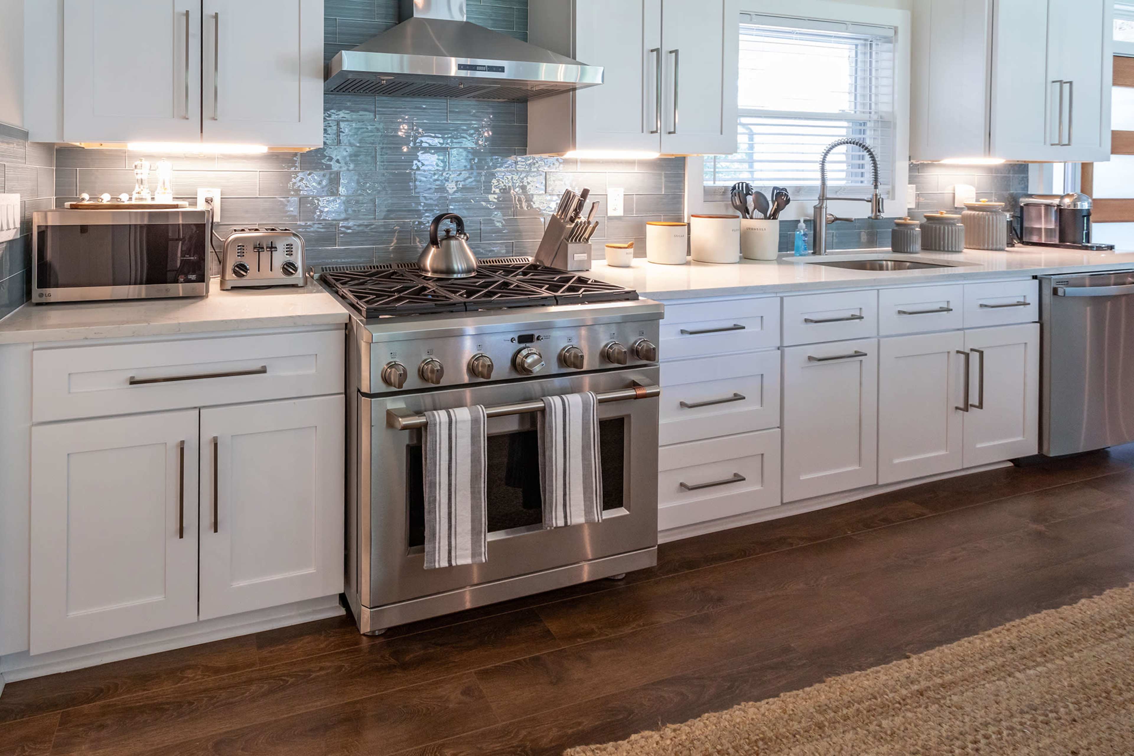 A modern kitchen features a stainless steel gas range, white cabinetry, and a tile backsplash, with various appliances and utensils neatly arranged.
