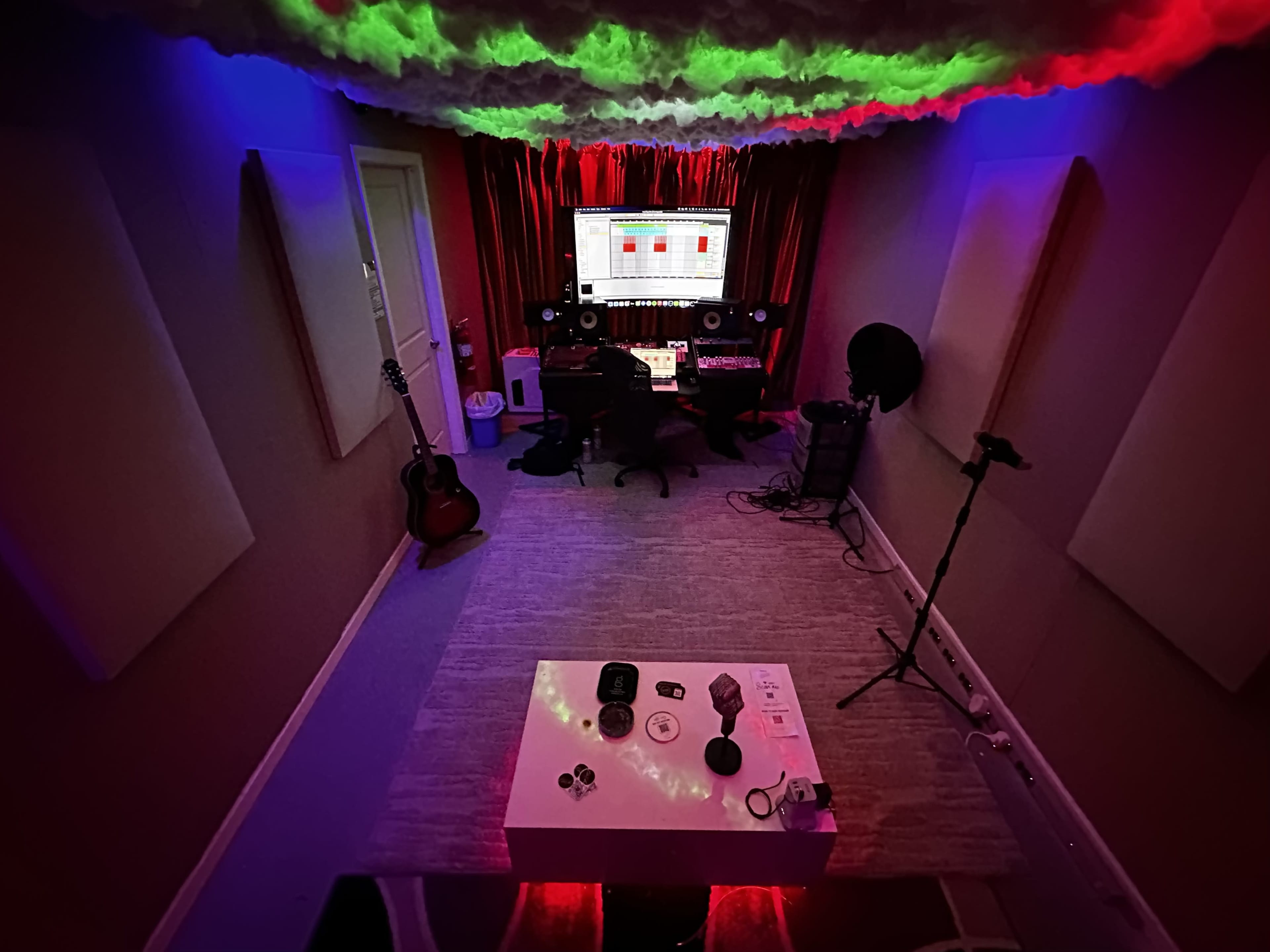 A music studio with a computer setup, musical instruments, and colorful lighting on the ceiling.