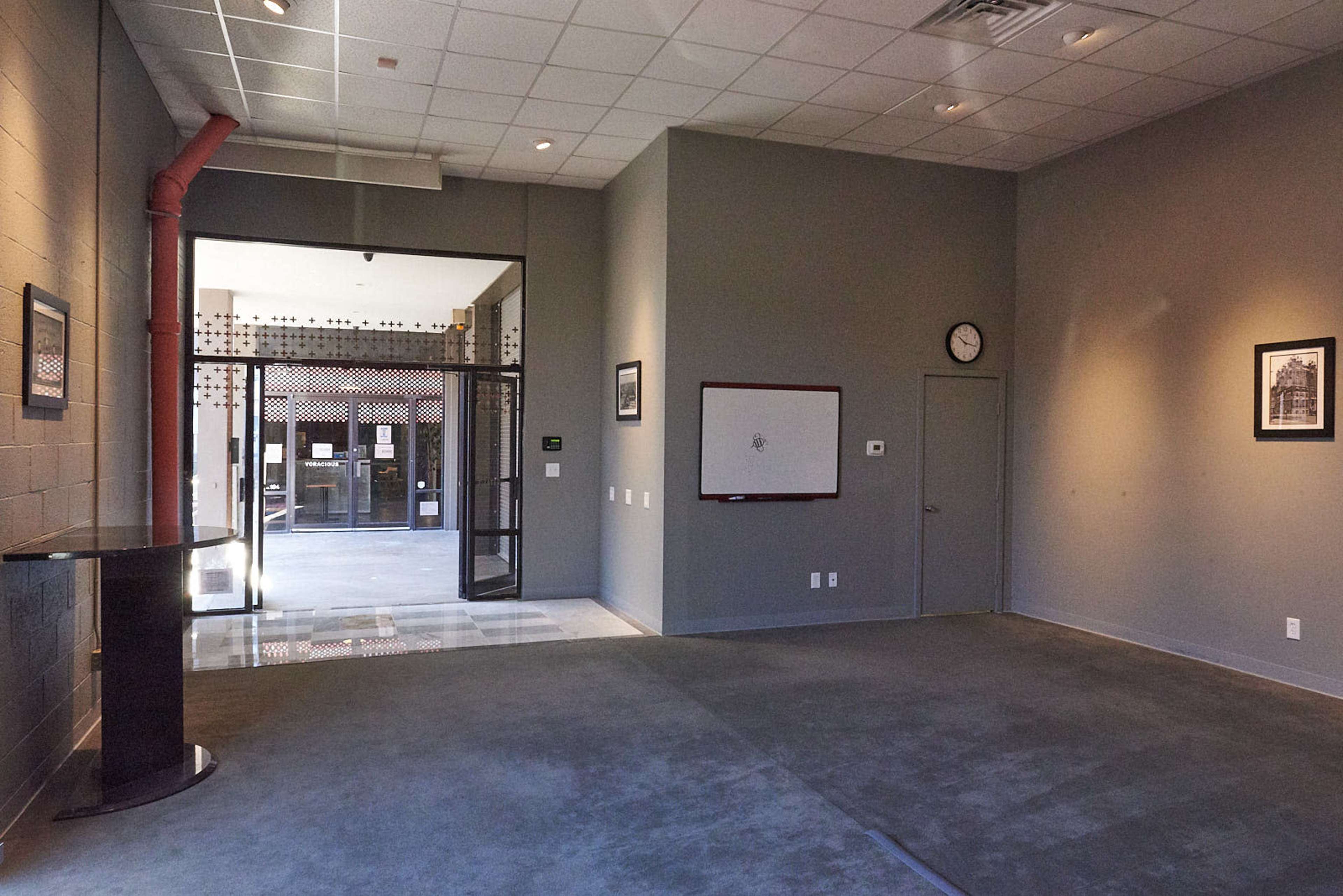 A spacious, semi-empty room with gray walls, a clock on the wall, and an entrance leading outside.