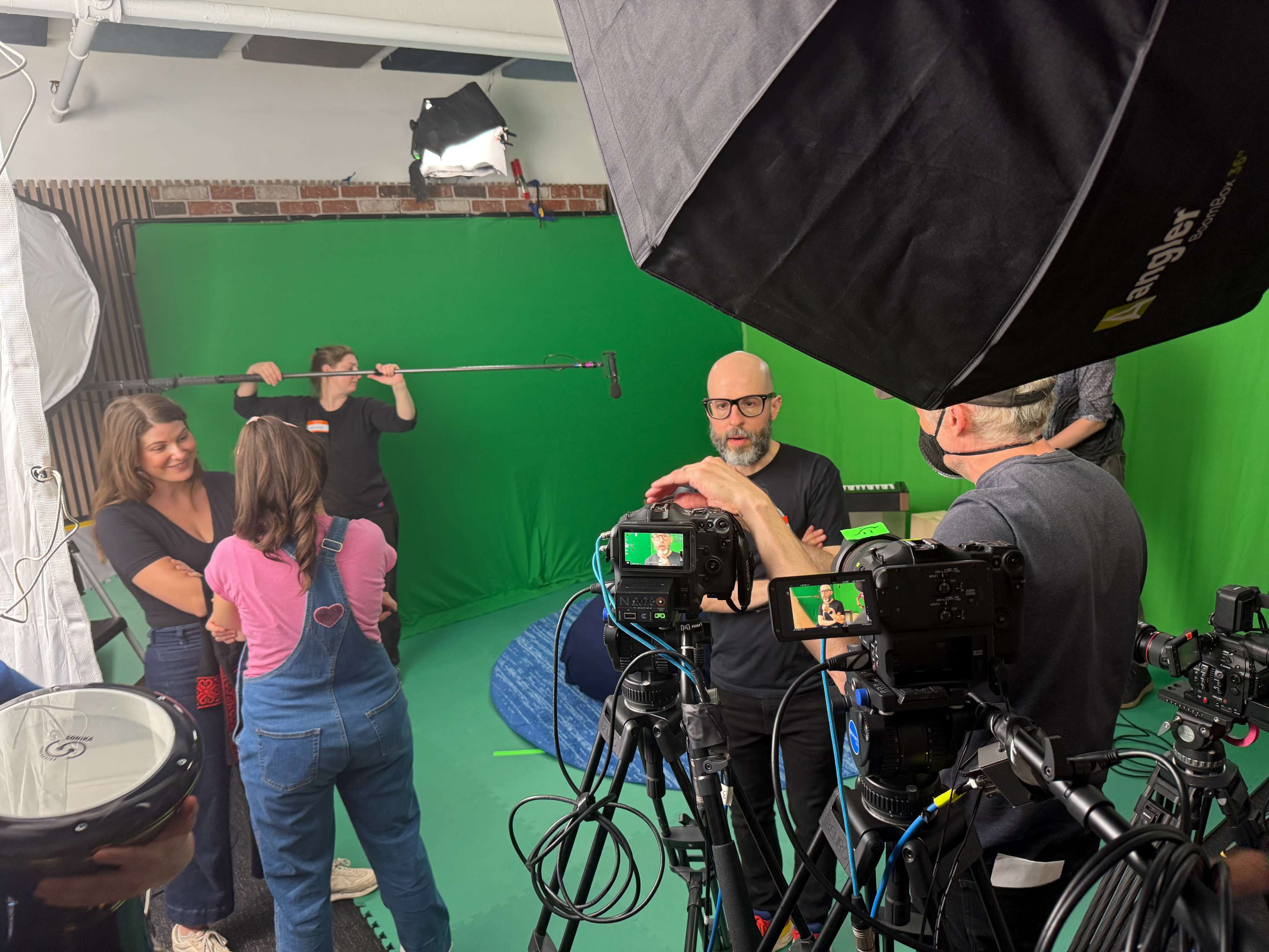 A group of people is in a studio equipped with green screens and various cameras, preparing for a shoot.