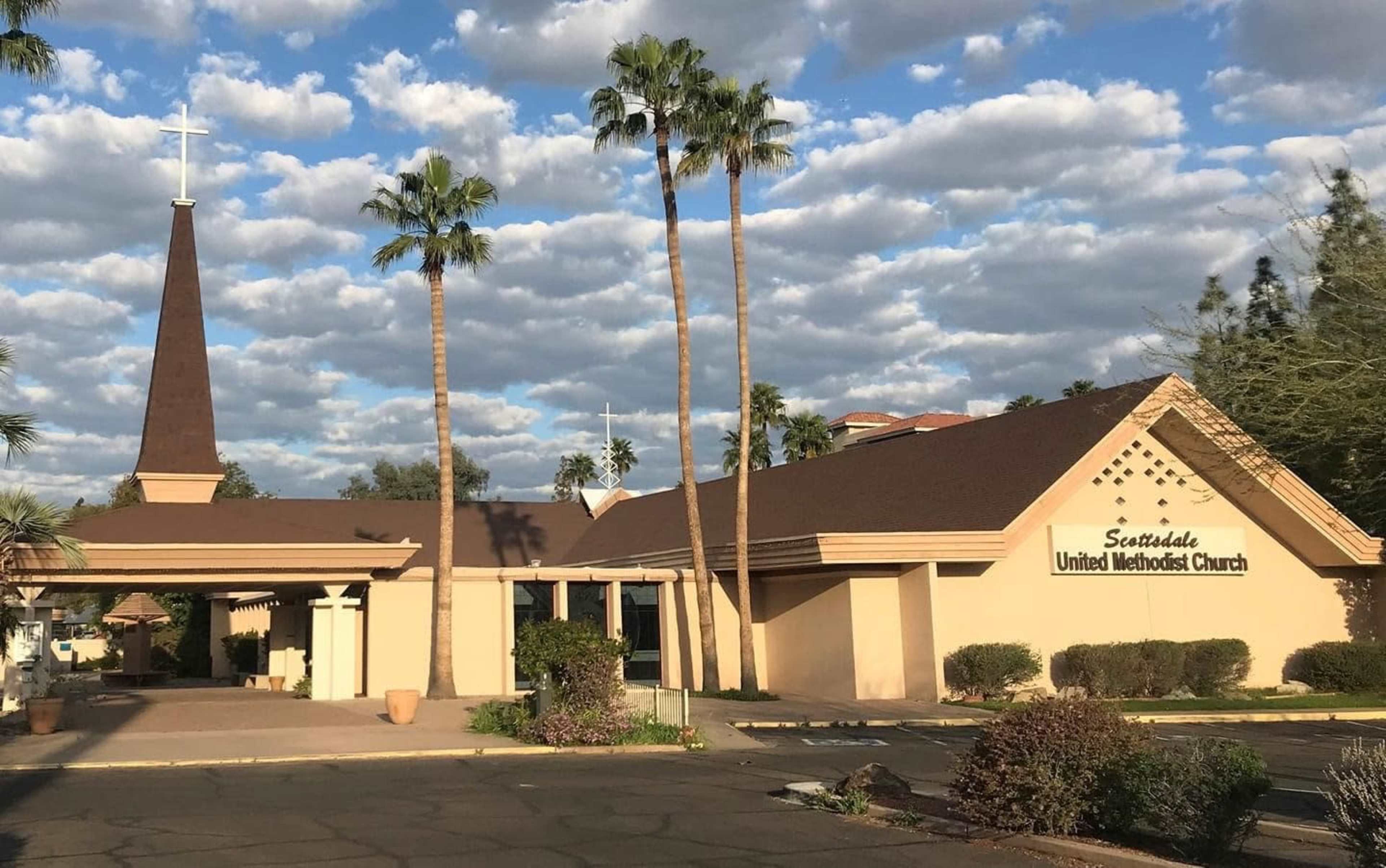 Scottsdale United Methodist Church with a tall steeple, surrounded by palm trees and a partly cloudy sky.