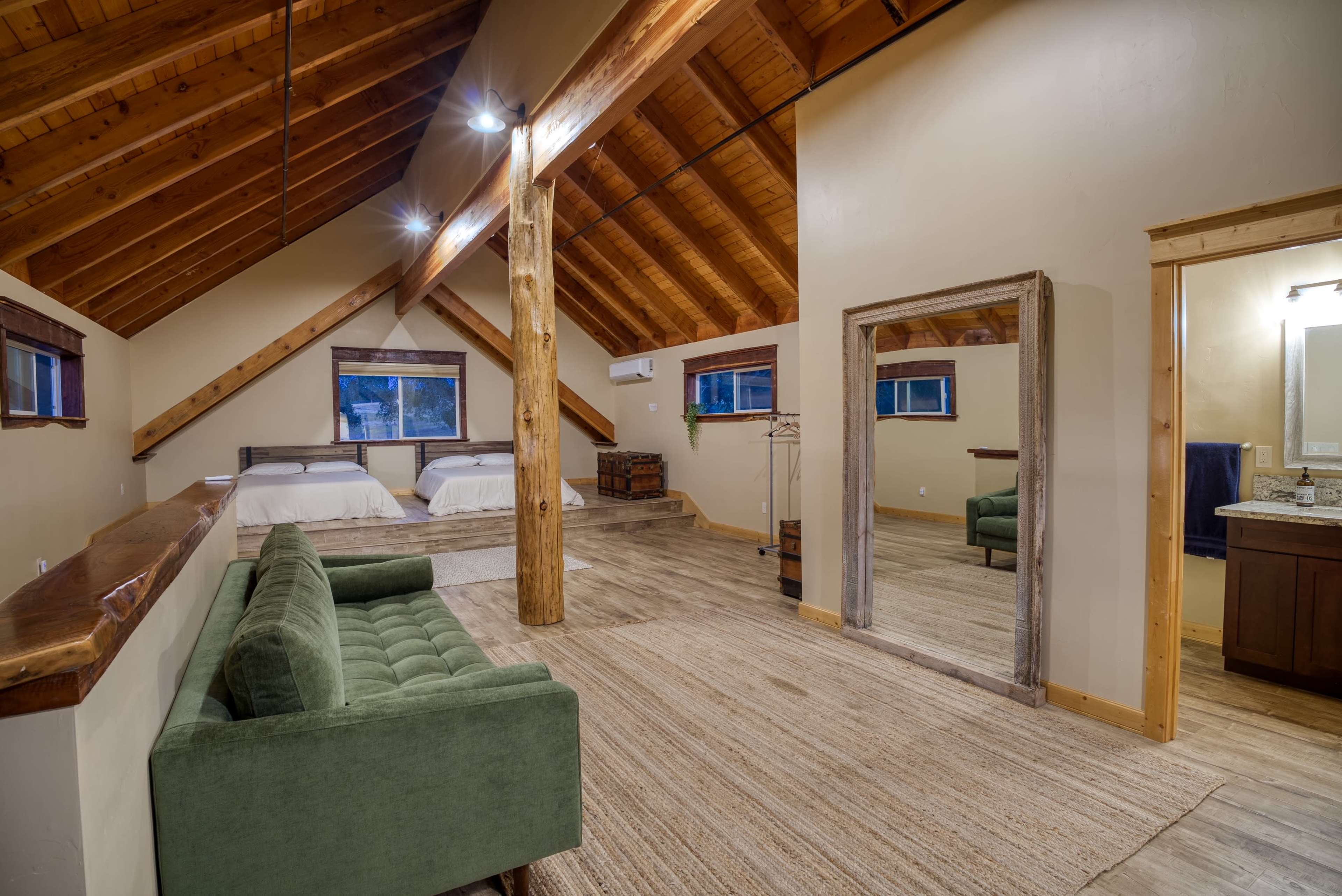 A spacious cabin room with two beds, a green sofa, a large mirror, and wooden beams on the ceiling.