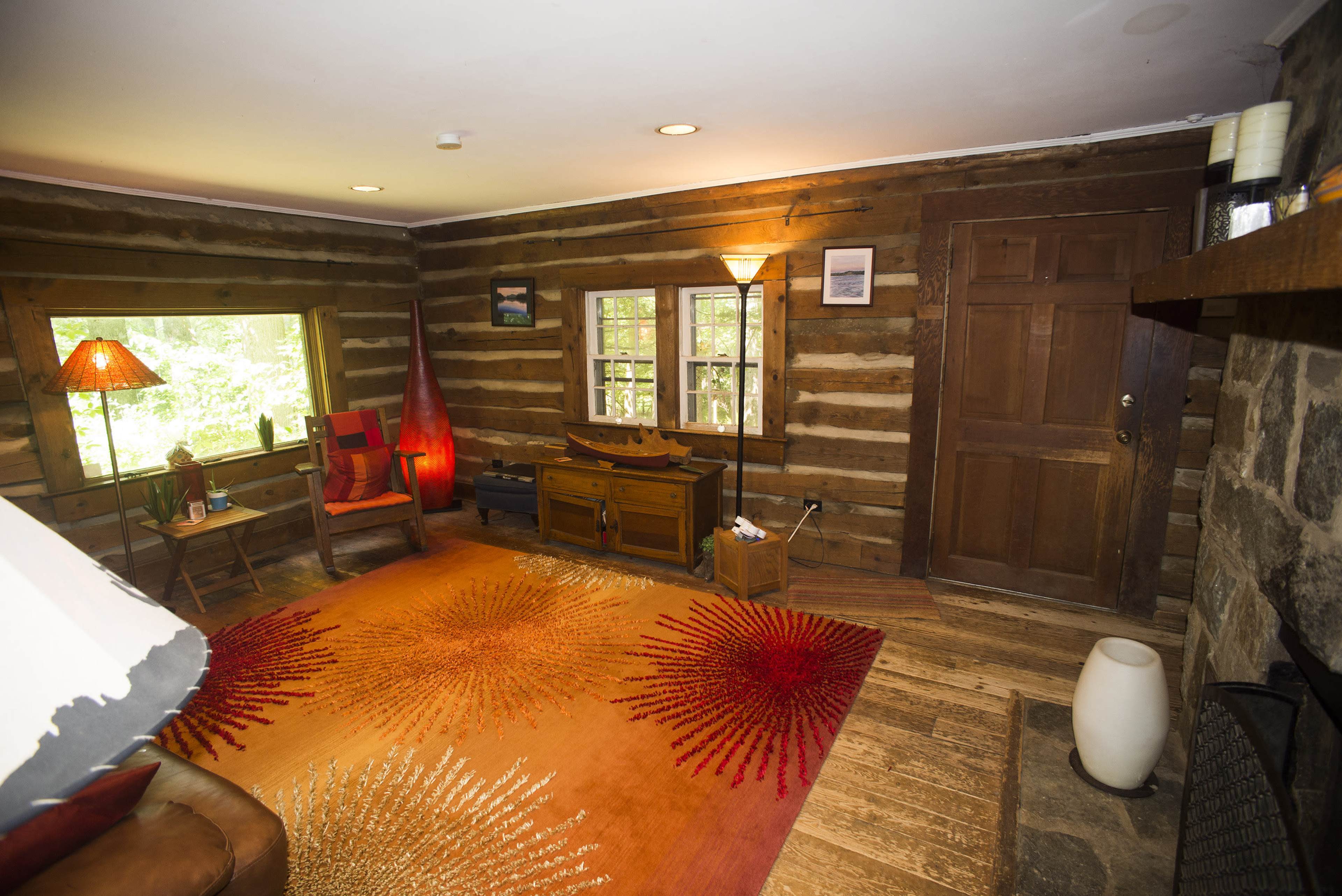 A cozy wooden cabin interior with a stone fireplace, a large rug, and a mix of wooden furniture.