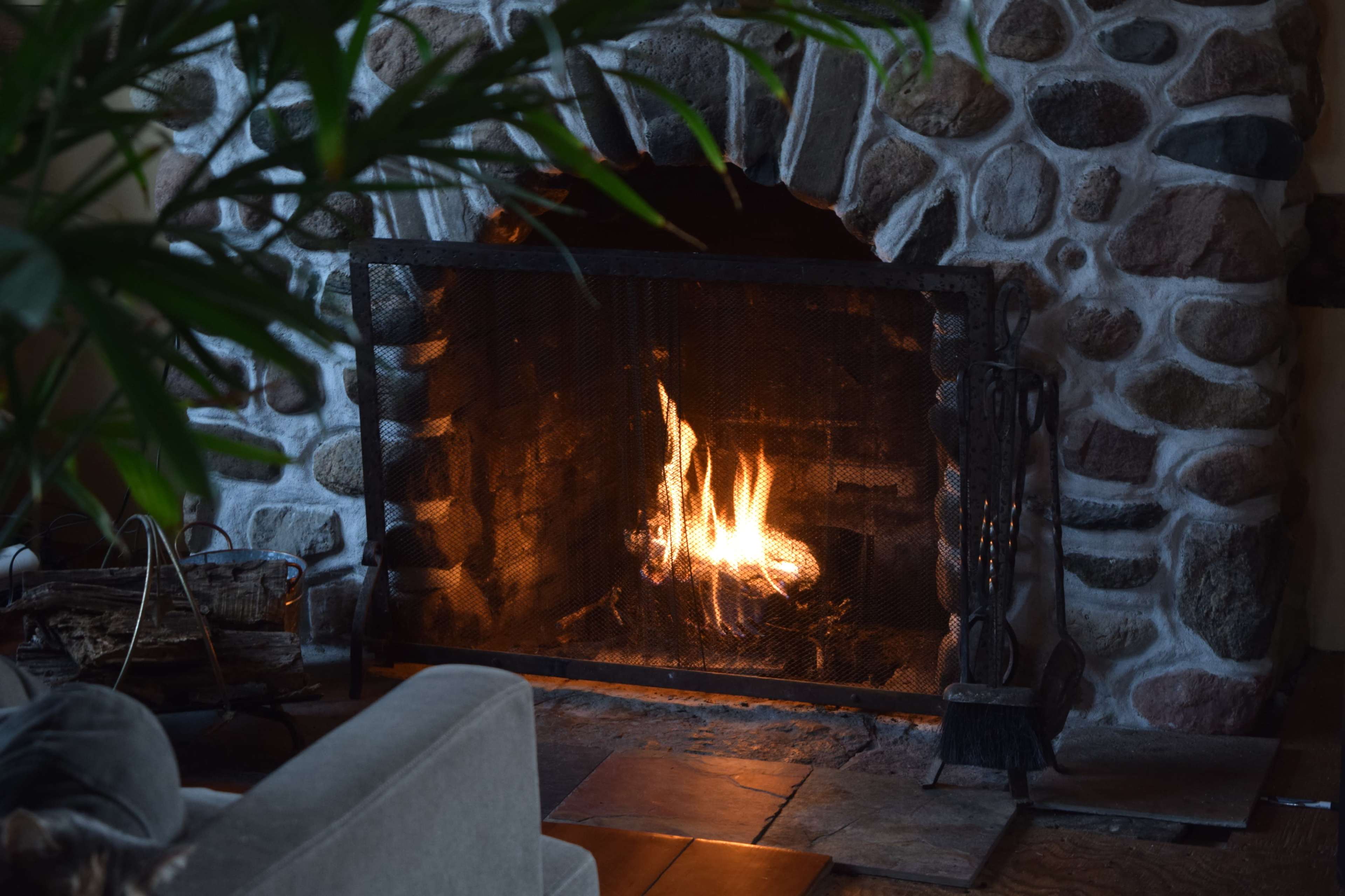 A stone fireplace with a mesh screen contains a small, flickering fire.