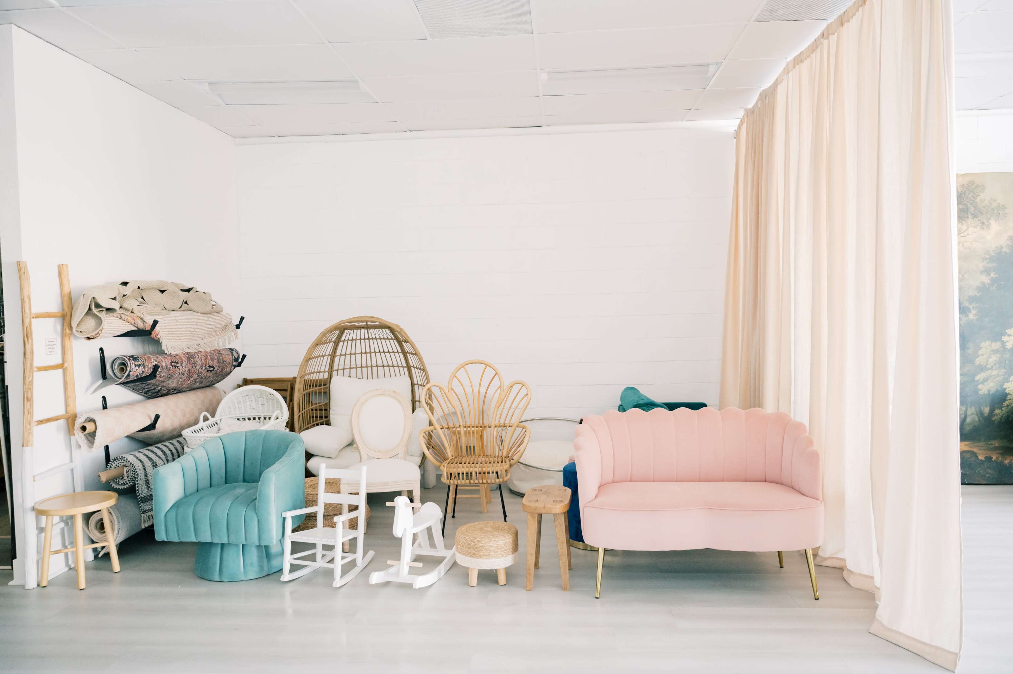 The image shows a bright, minimalistic interior with various furniture pieces, including colorful chairs and a pink couch, arranged against a white wall.