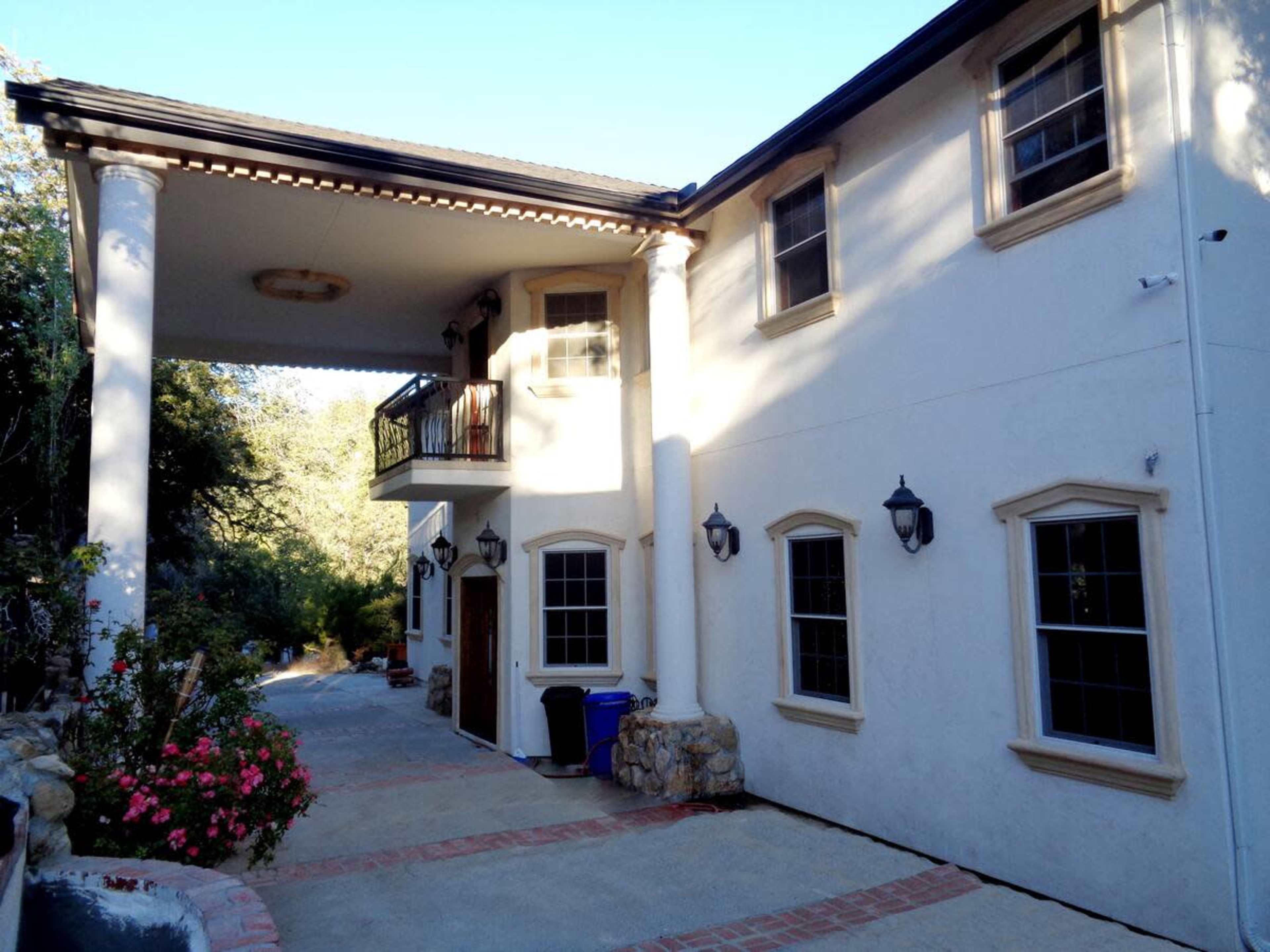 The image shows a two-story house with a large covered entrance, columns, and a landscaped pathway leading to it.