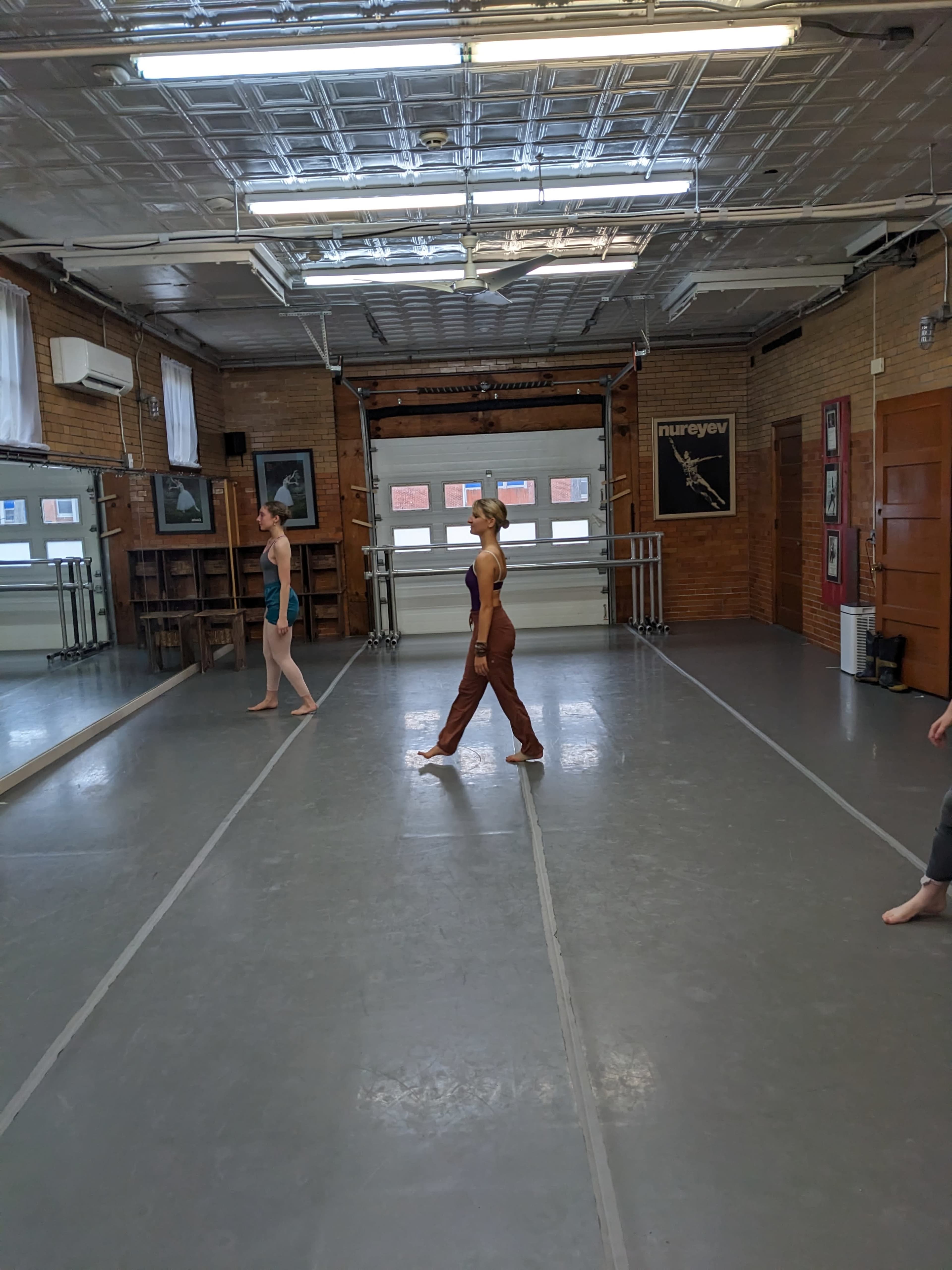 Two dancers practice in a mirrored dance studio with wooden accents and large windows.