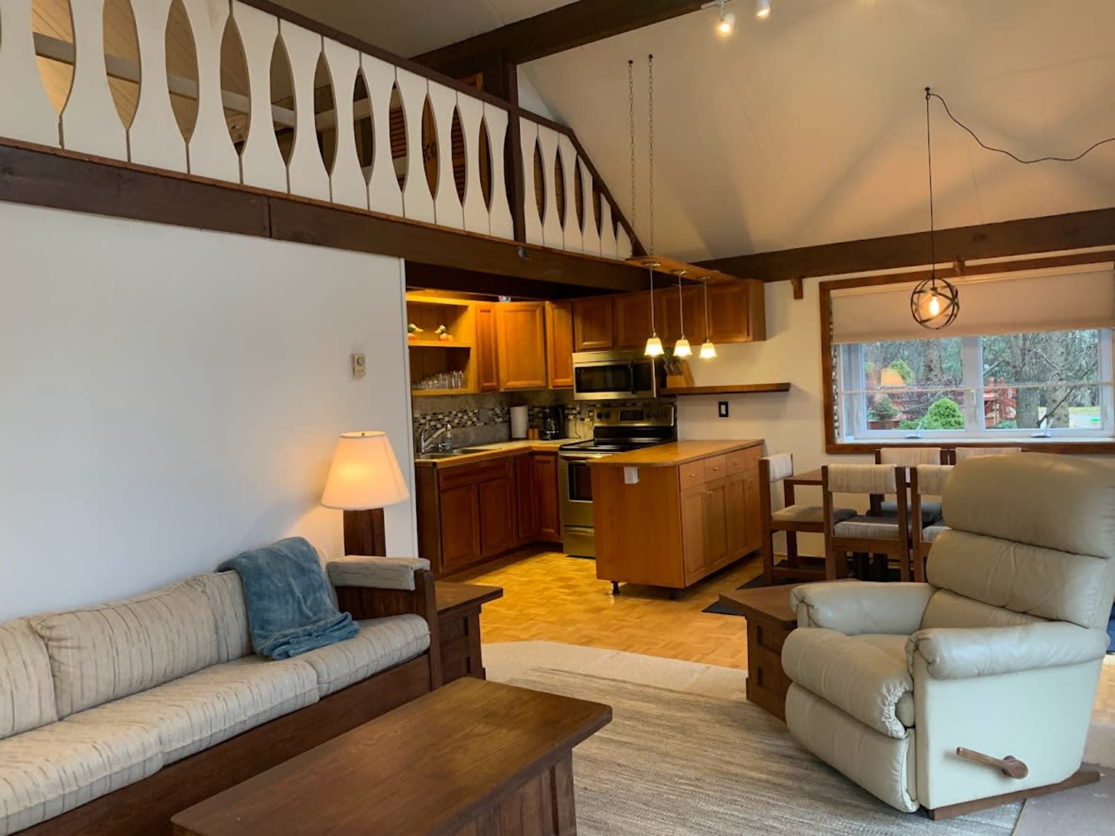 A cozy living area with a sofa and recliner, adjacent to a kitchen fitted with wooden cabinets and modern appliances.