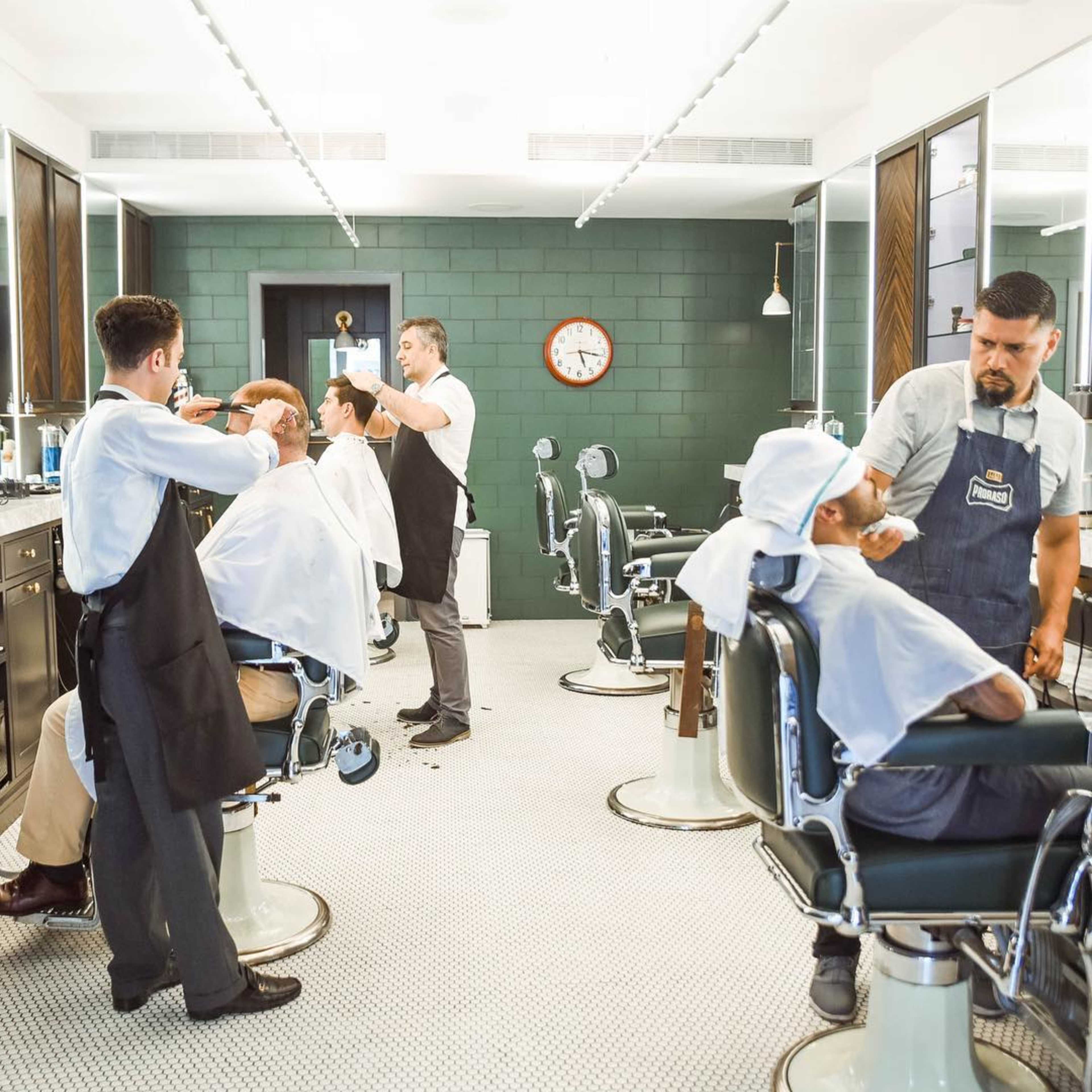 A modern barbershop with several barbers tending to clients in vintage-style chairs.