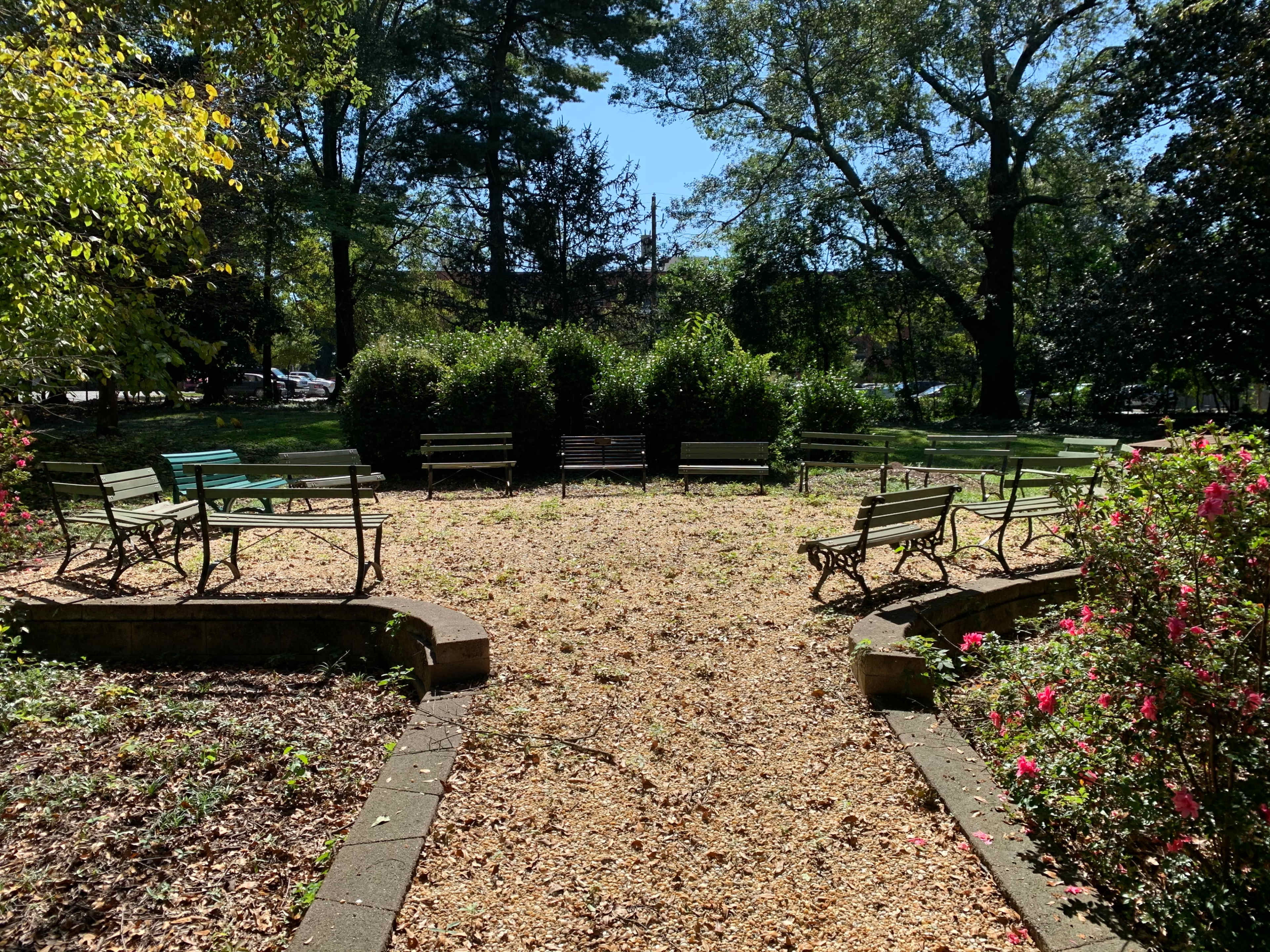 The image shows a circular garden area surrounded by benches and greenery, with a ground covered in fallen leaves.