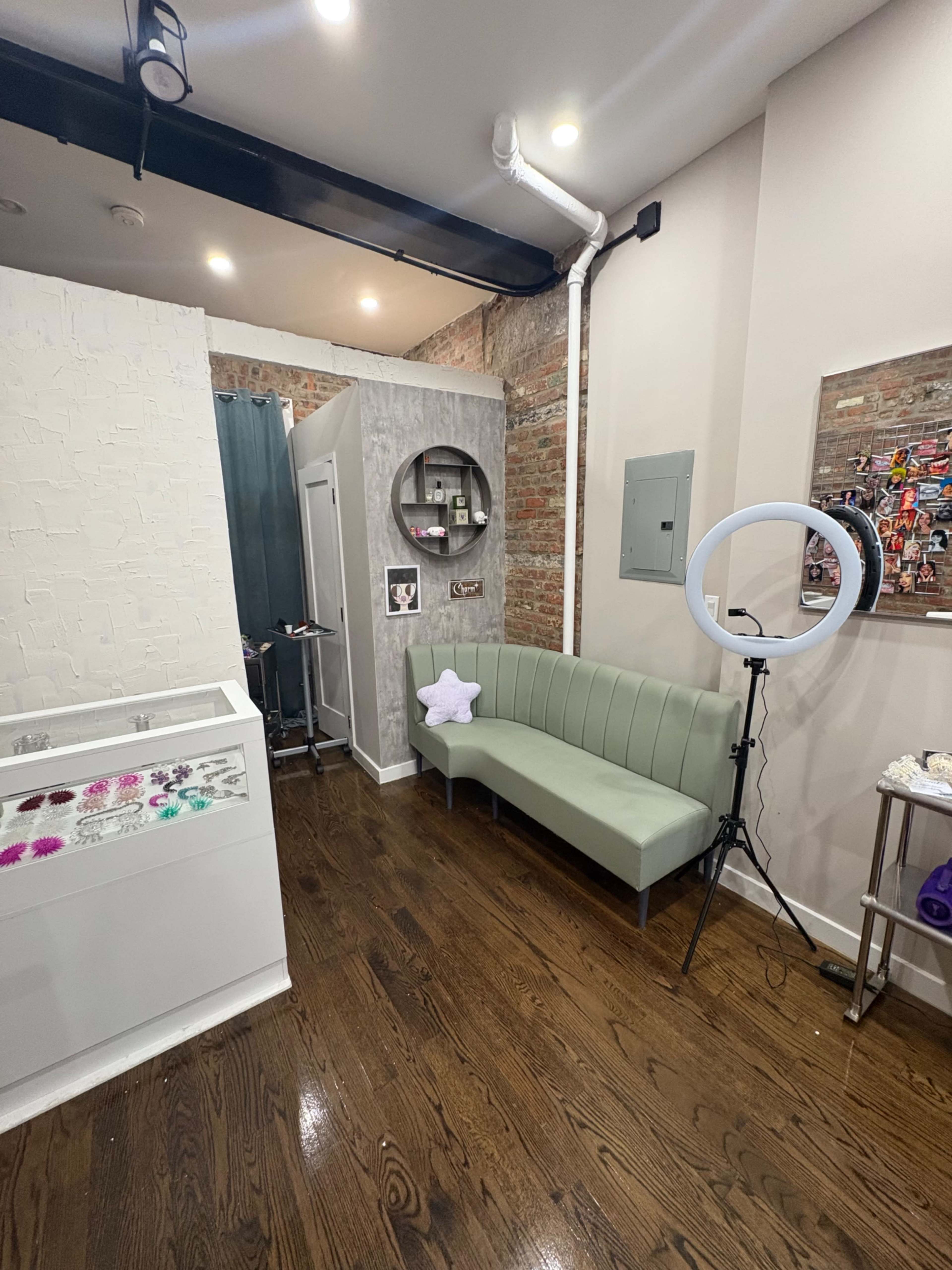 The image shows a modern interior featuring a green upholstered bench, a circular mirror, a ring light on a tripod, and a partially visible wall with exposed brick.