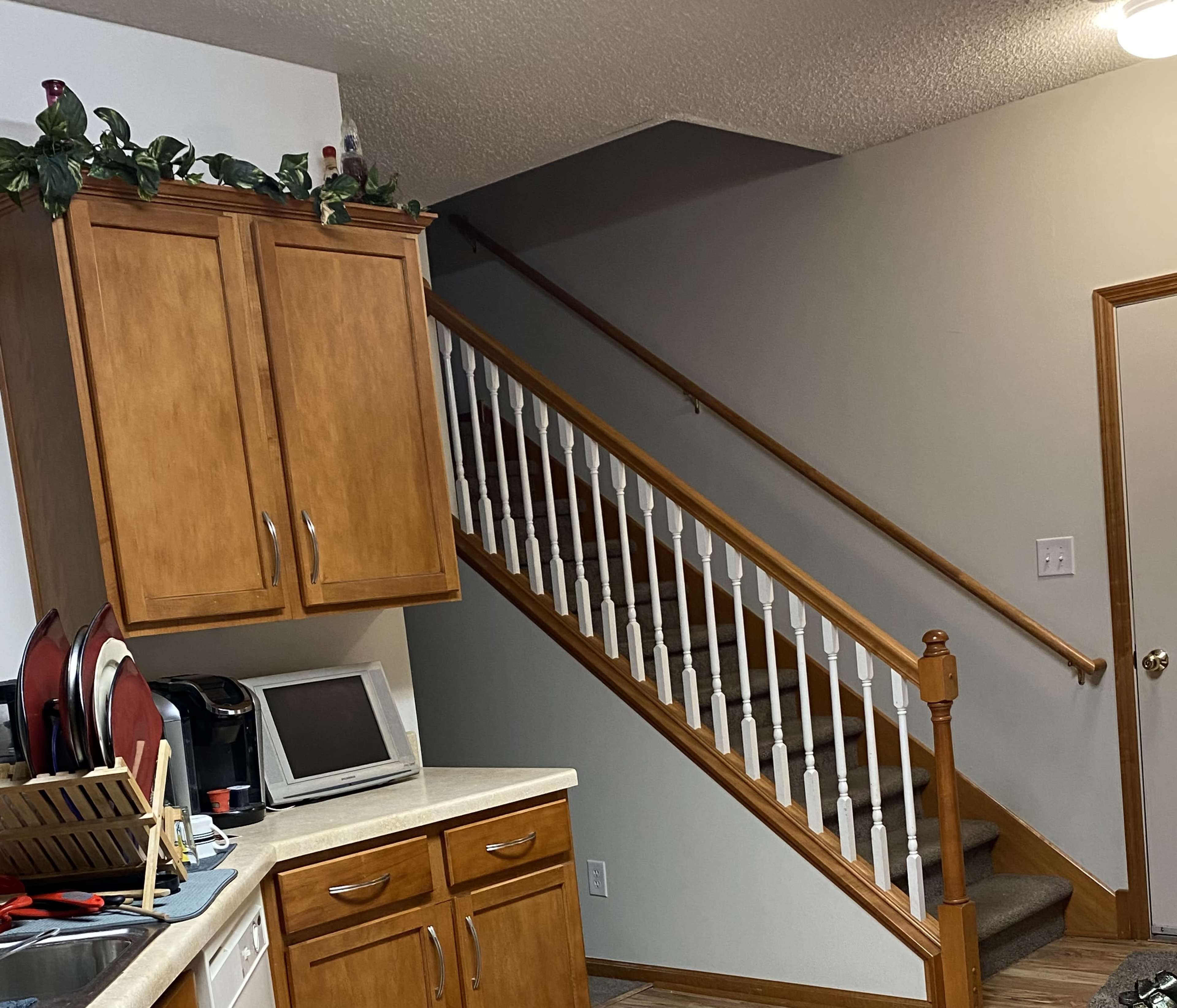A kitchen area with wooden cabinets, a countertop, and a staircase leading to an upper floor.