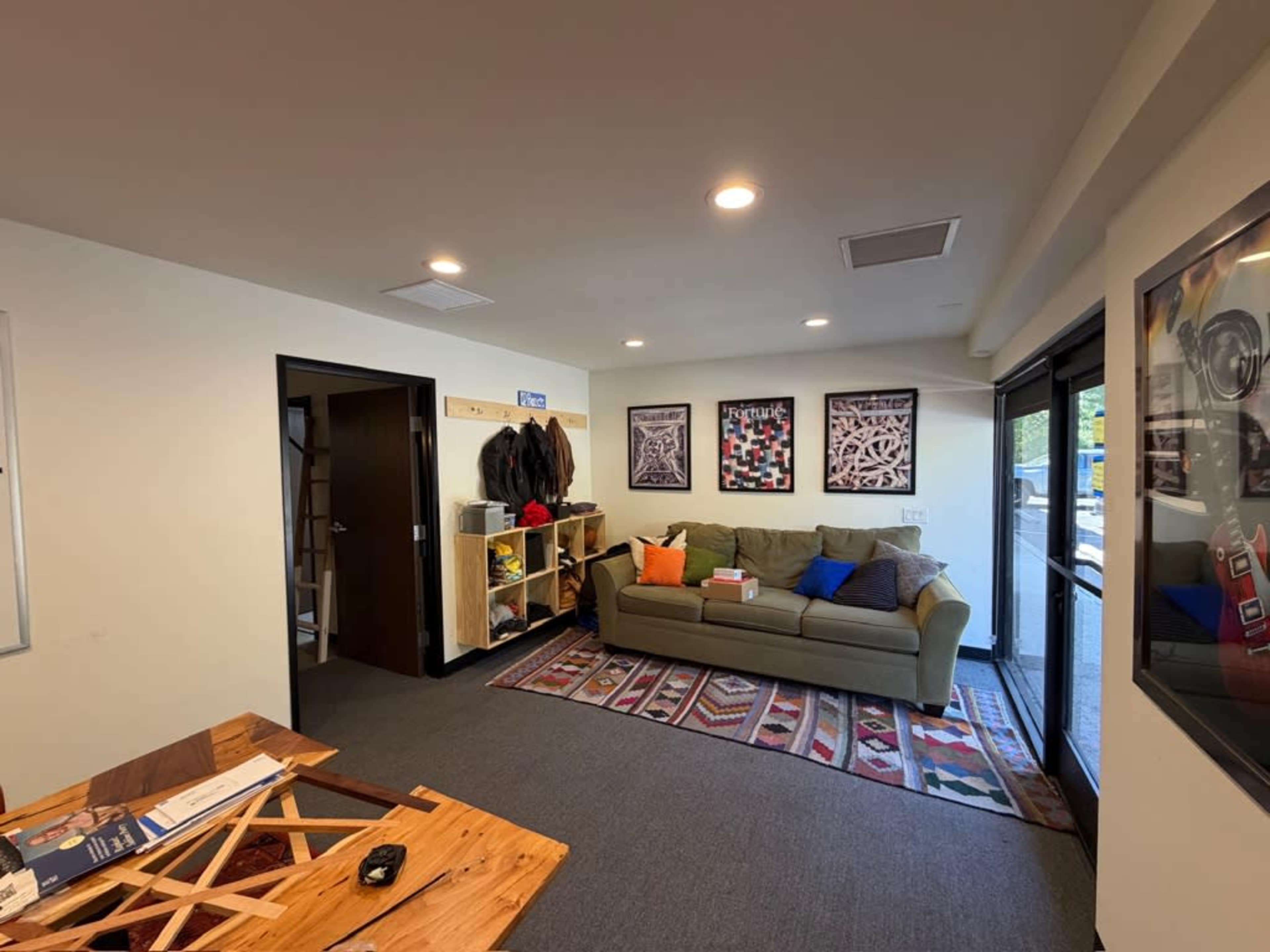 The image shows a modern office space featuring a green couch, a wooden table, and decorative artwork on the walls.