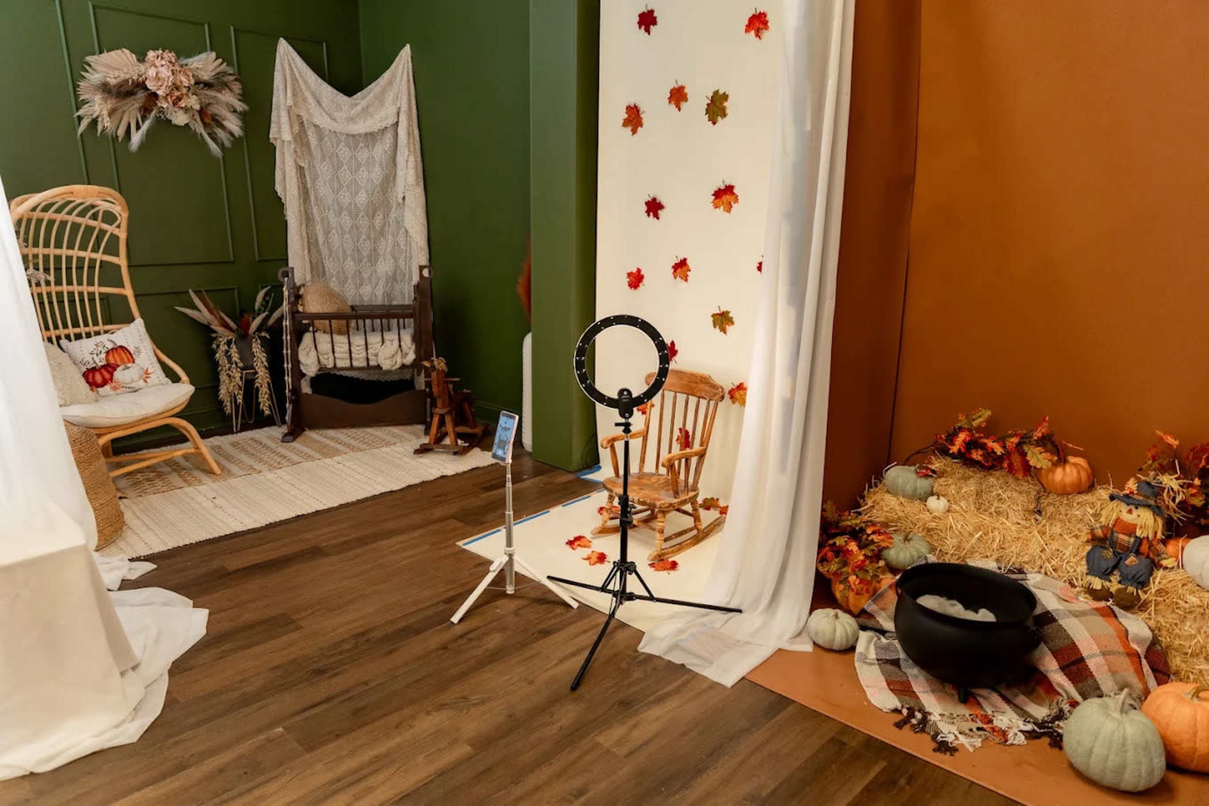 The image shows a cozy indoor scene decorated with autumn leaves and pumpkins, featuring a ring light on a stand and a rocking chair near a wall draped in fabric.