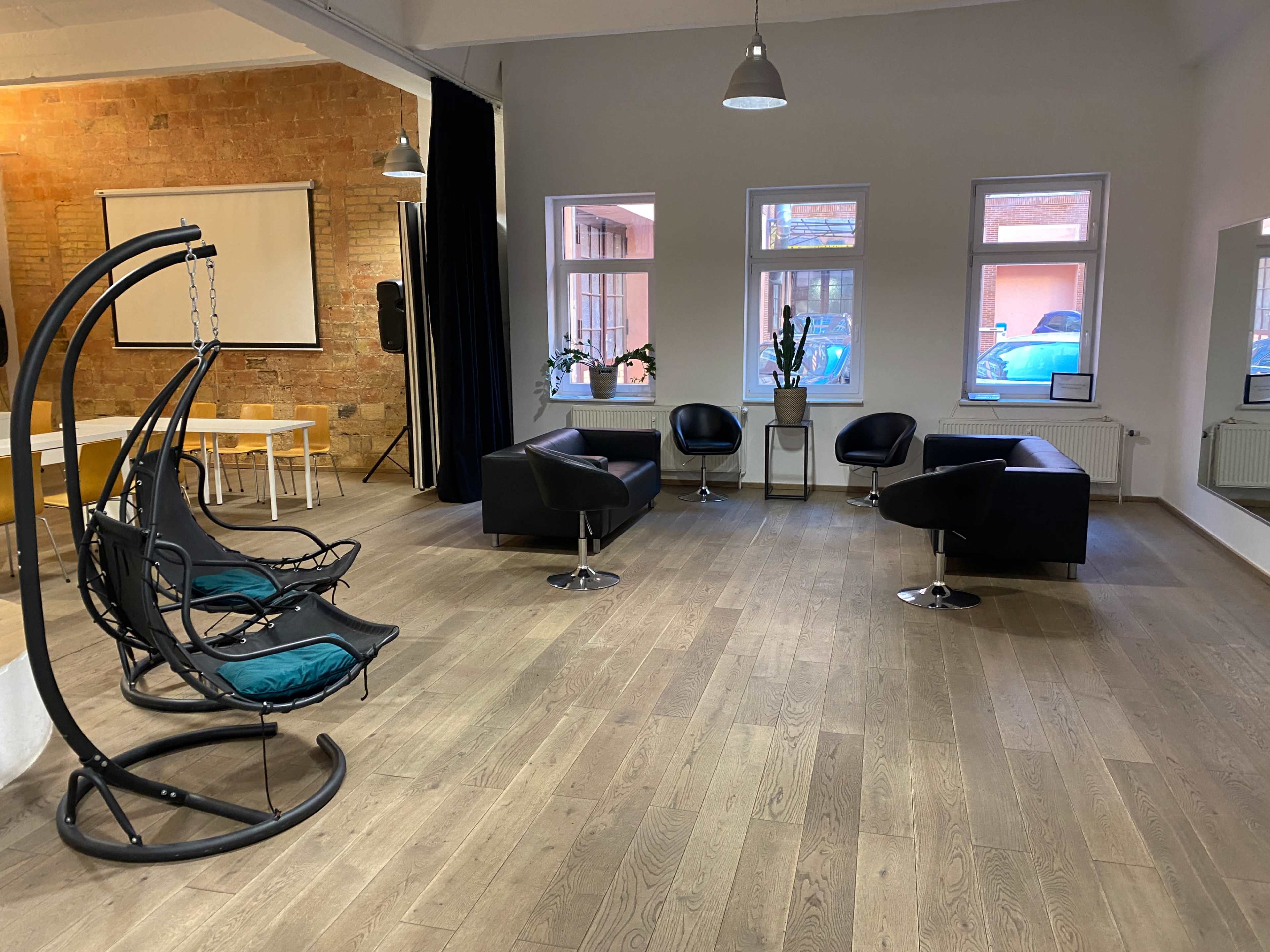 The image shows a spacious, modern lounge area with multiple seating options, including two hanging chairs and four armchairs, along with large windows and a wooden floor.