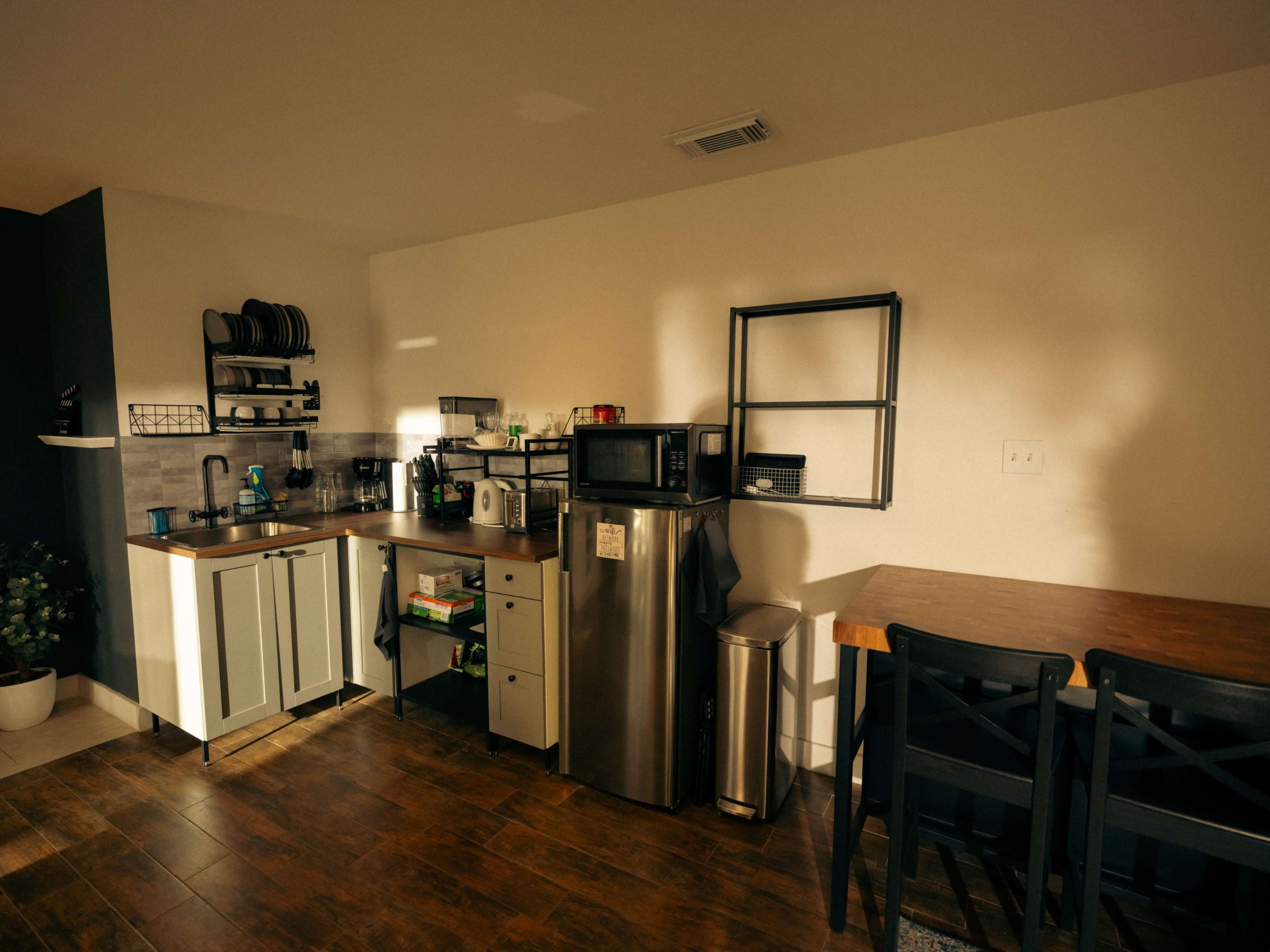 The image shows a modern kitchen with stainless steel appliances, a wooden dining table, and a well-organized countertop.