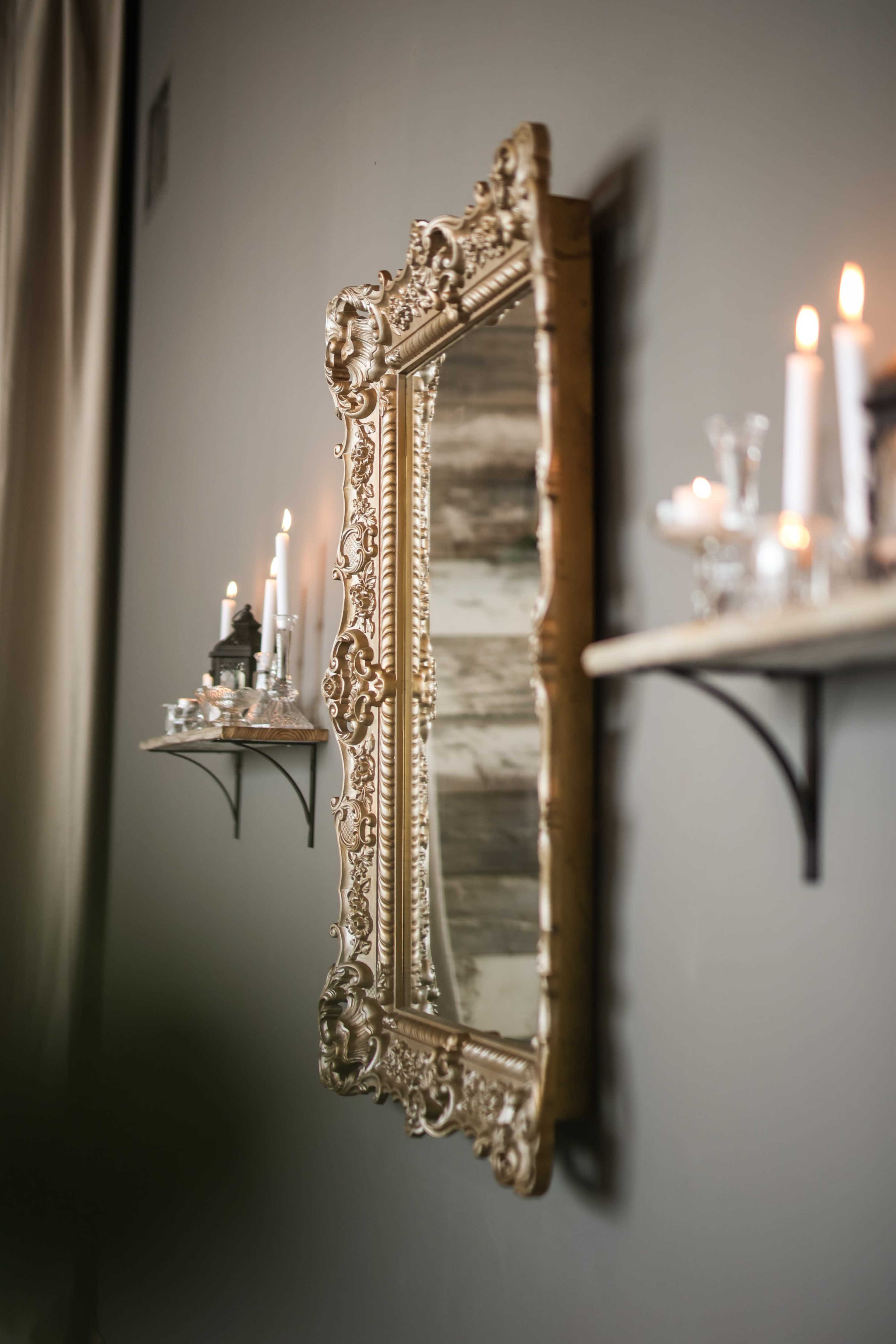 An ornate gold mirror hangs on a wall beside shelves adorned with candles and decorative items.