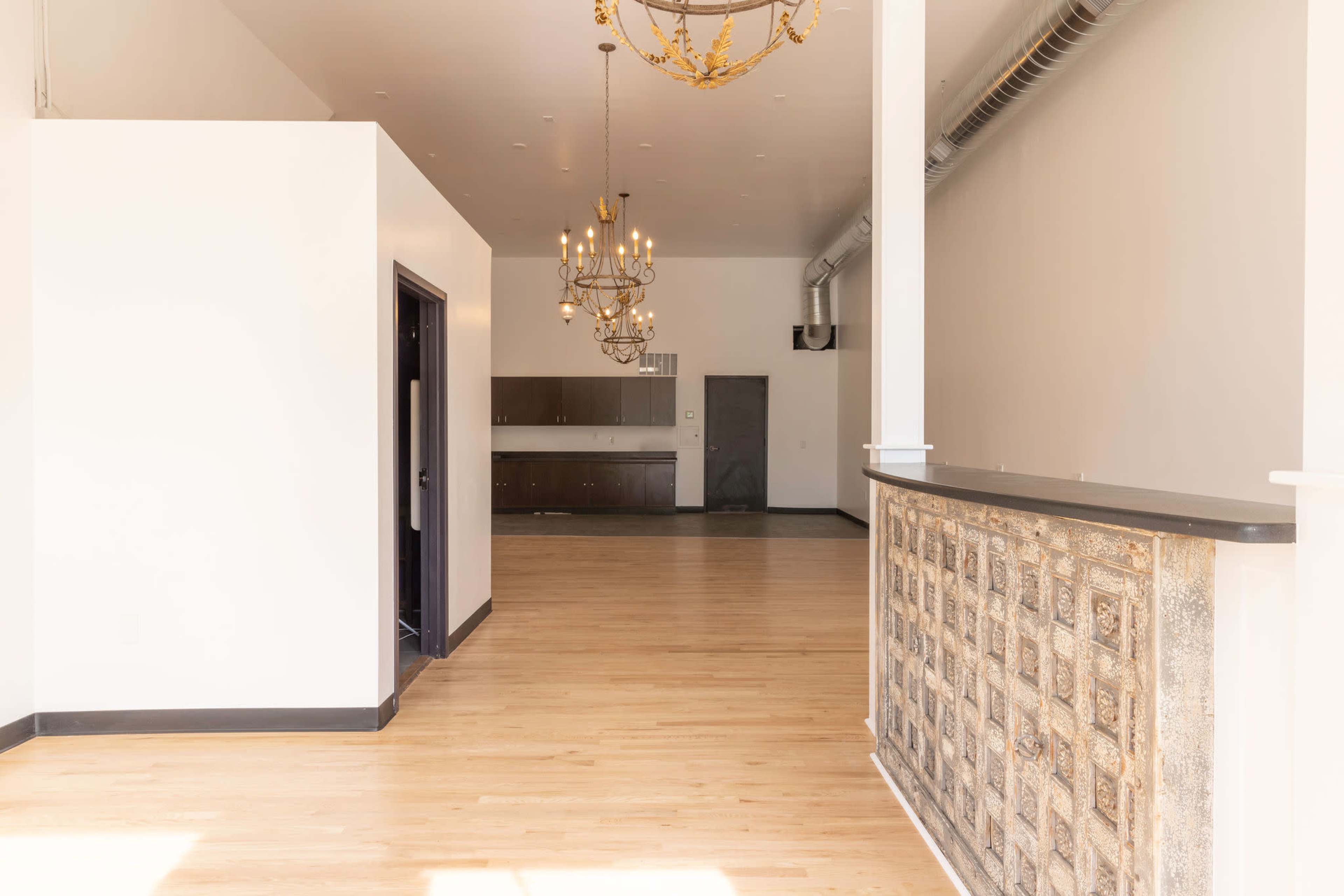 A spacious, empty interior with wooden flooring, a decorative reception counter, and a chandelier above.