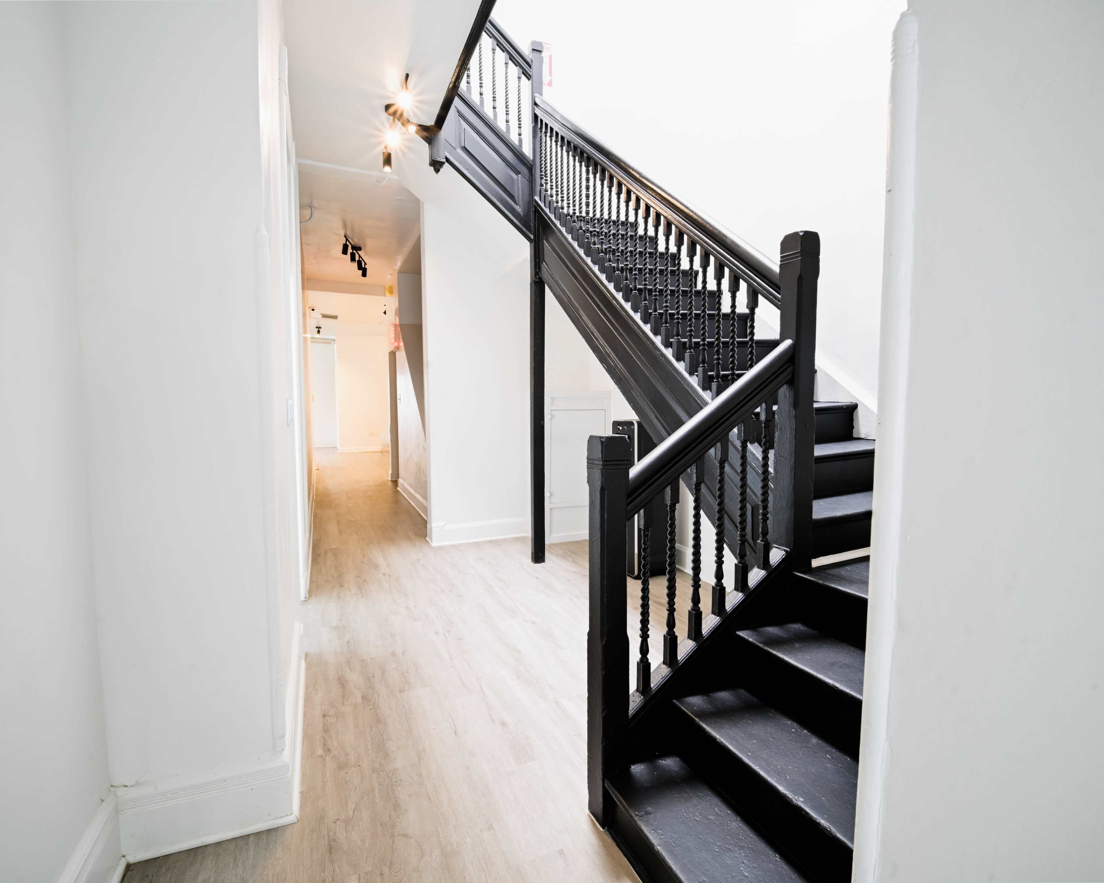 A well-lit hallway features a black staircase with a wooden banister leading to an upper floor.
