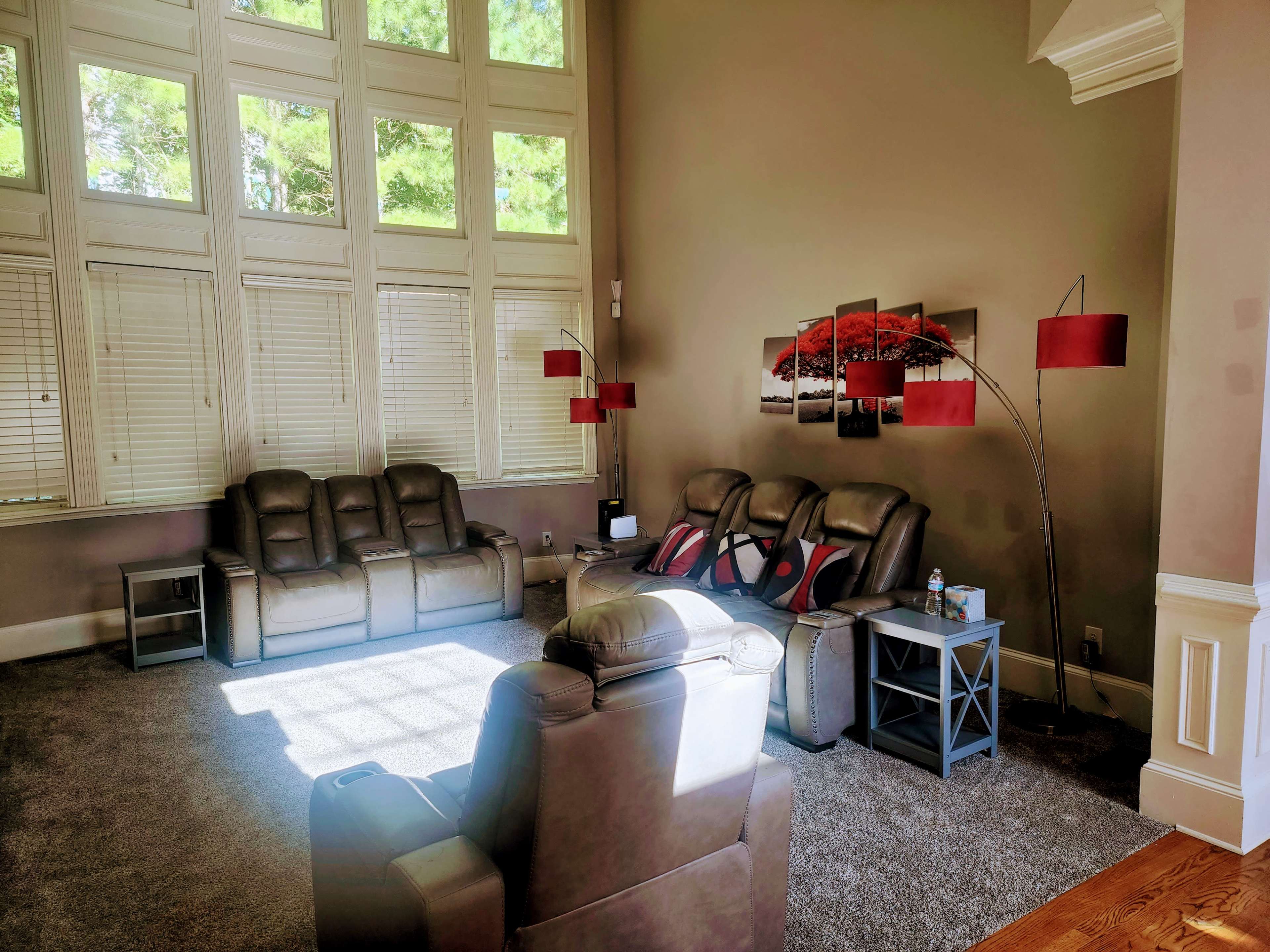 The living room features large windows that allow natural light to illuminate a seating area with gray recliners and side tables.