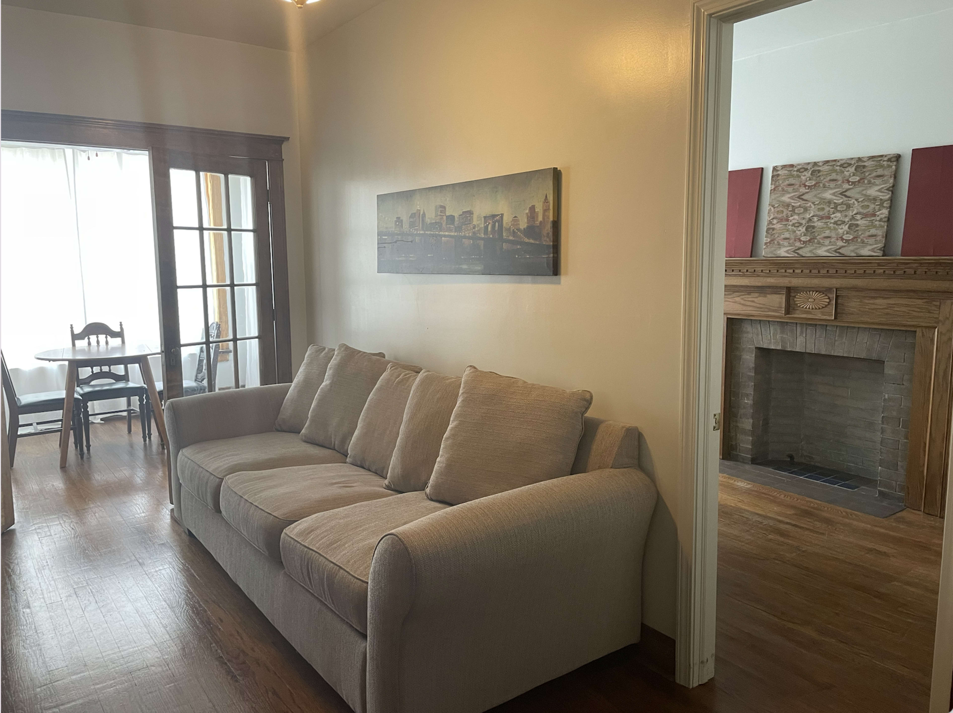 A living room with a beige sofa, a fireplace, and a dining area visible through a set of glass doors.