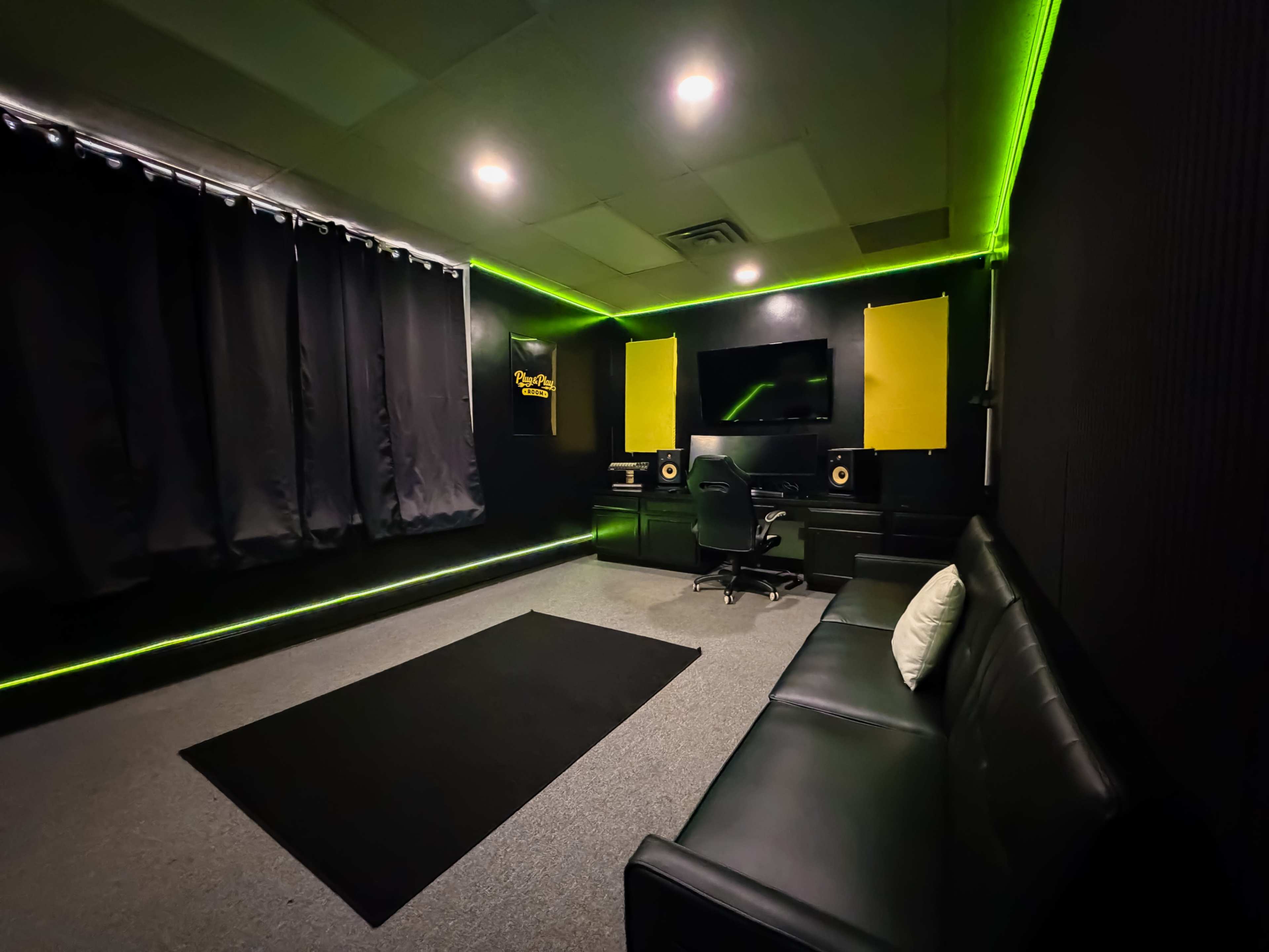The image depicts a music production studio featuring a black couch, a chair with a desk, sound monitors, and dim lighting with green neon accents.