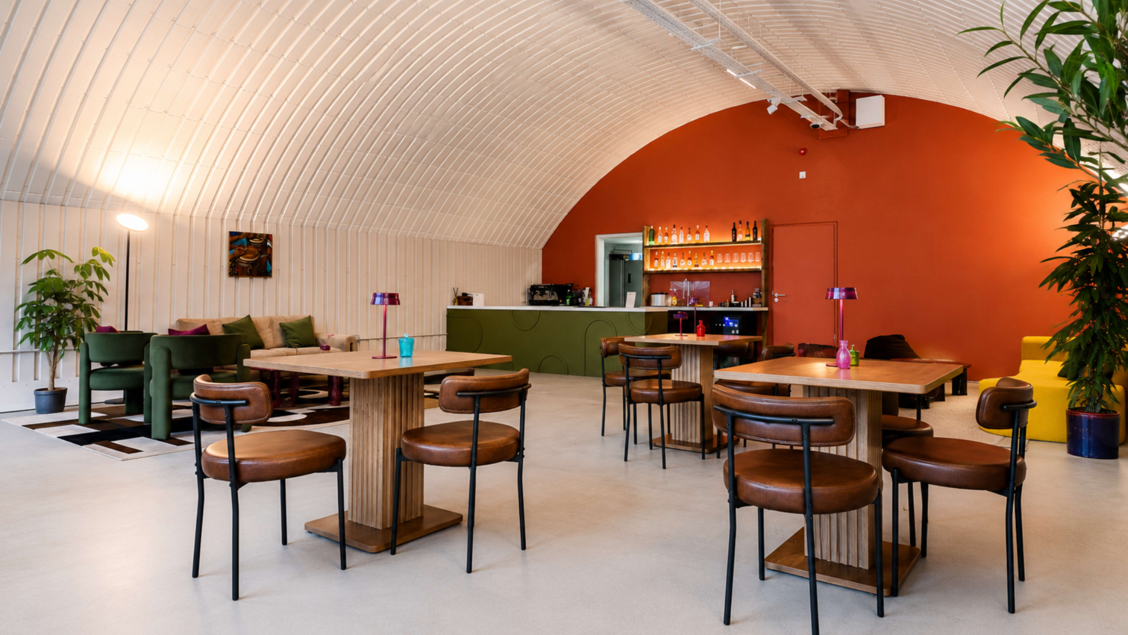 The image features a modern café interior with wooden tables and chairs, a bar area in the background, and leafy plants decorating the space.