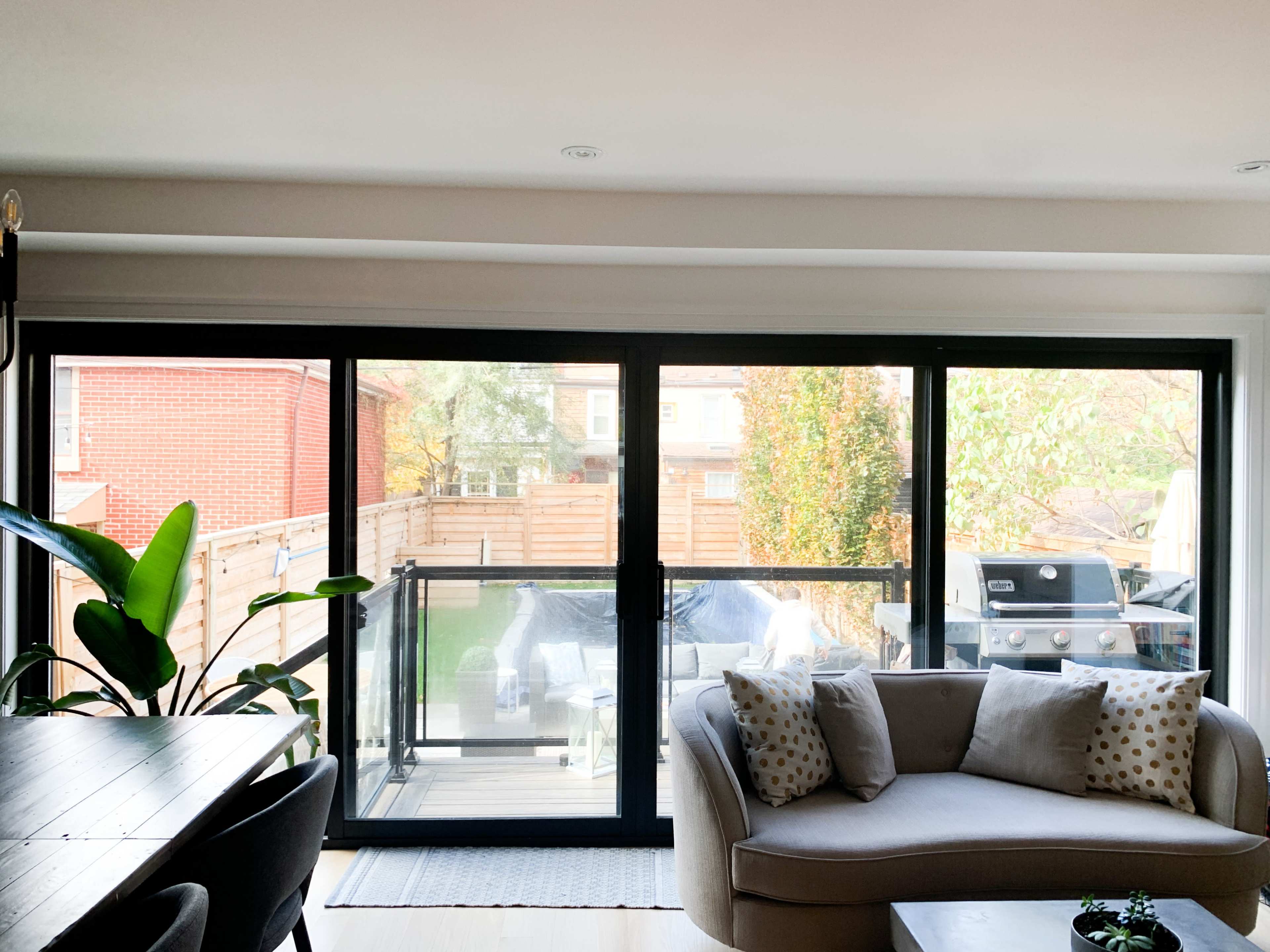 A modern living room features a large sliding glass door that opens to a deck with outdoor seating and a barbecue grill.