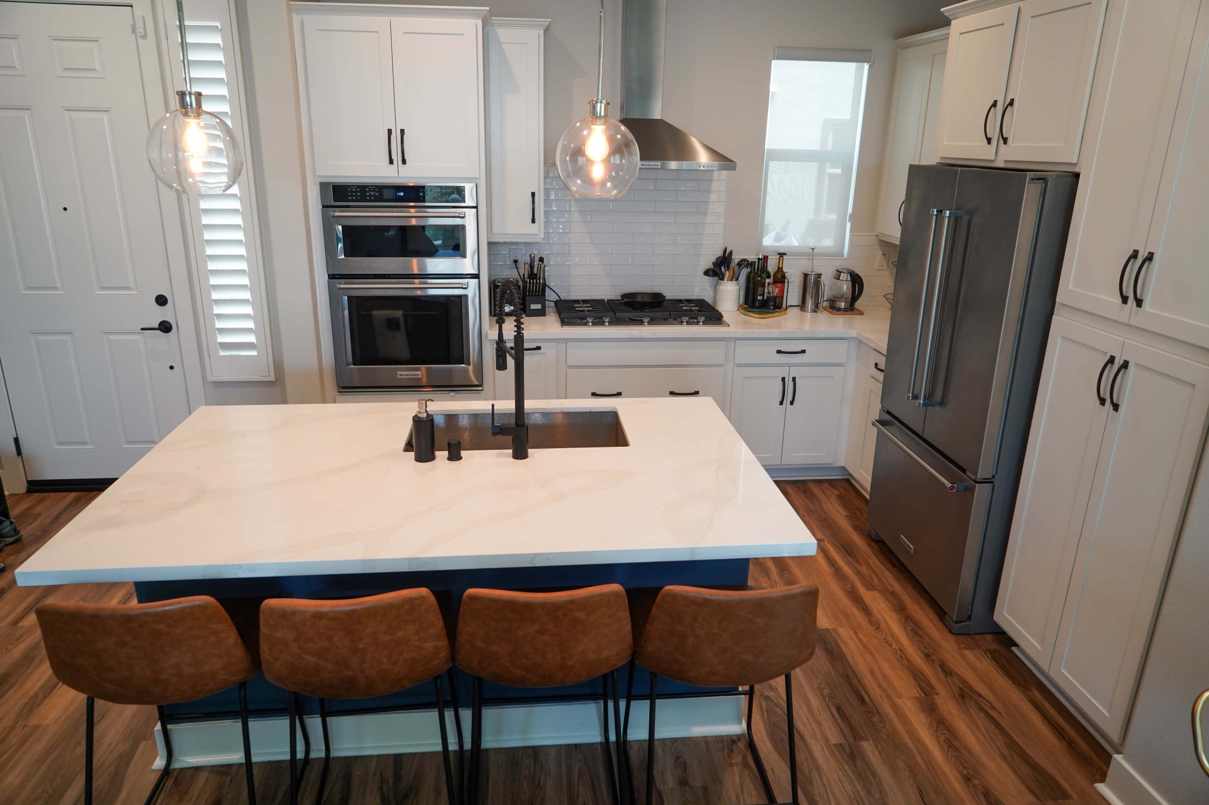 A modern kitchen featuring white cabinets, a large island with a sink, and four brown barstools.