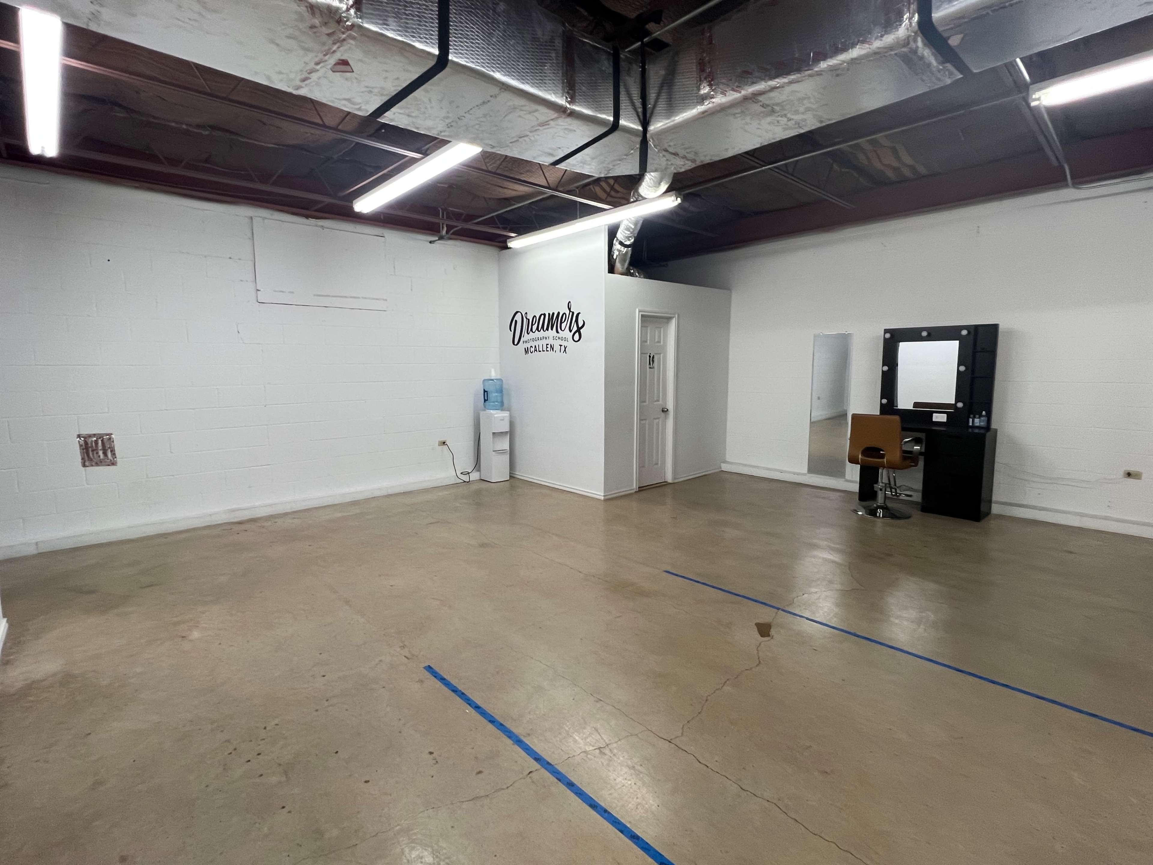 A spacious, empty salon area with a water cooler, a mirror, and a styling chair against one wall.