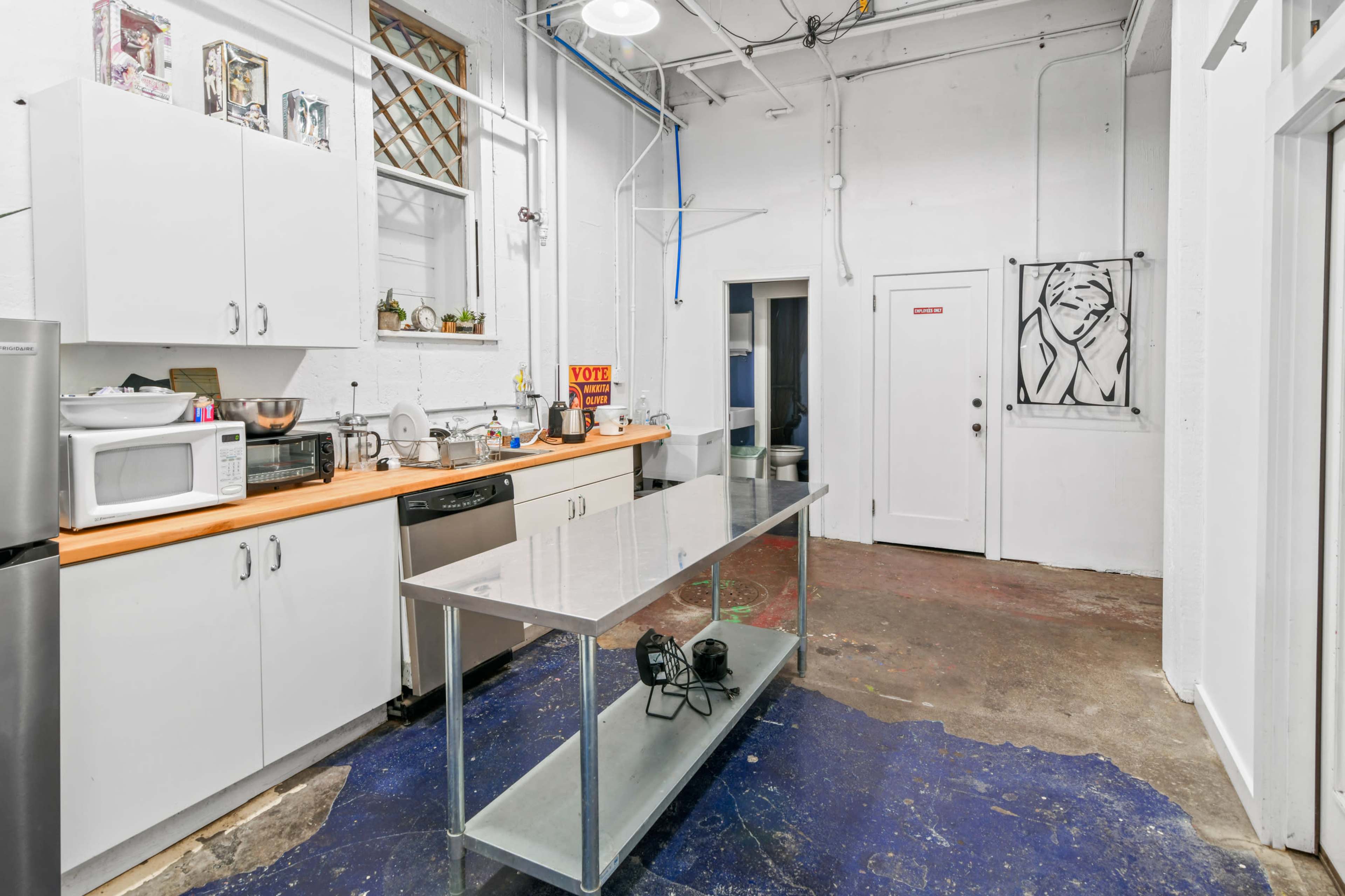 A kitchen area with white cabinets, a stainless steel table in the center, and various kitchen appliances against the wall.