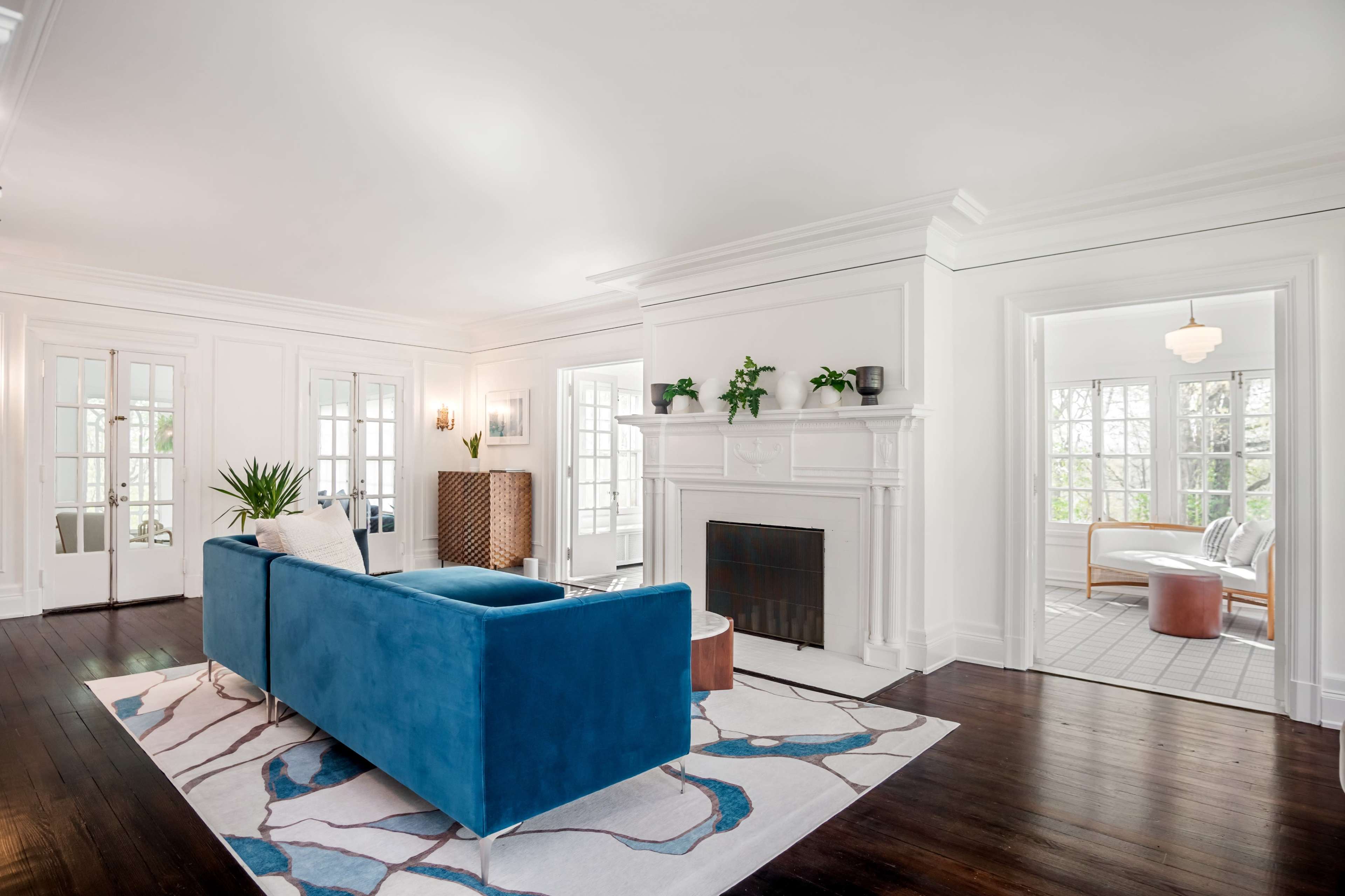 A bright, airy living room with a blue couch, a large area rug, and white walls, featuring a fireplace and clear views into adjacent rooms.