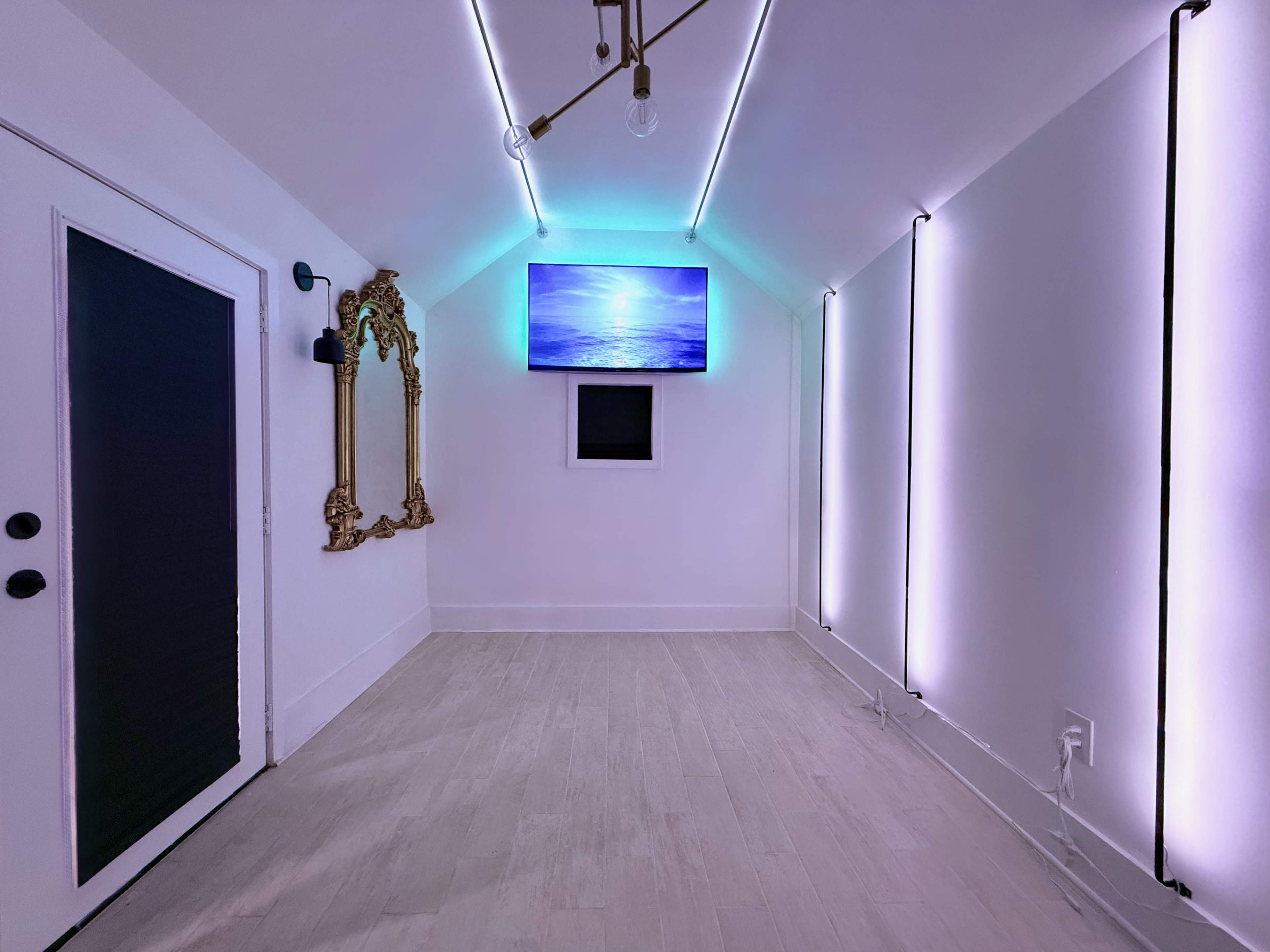 The image shows a bright, minimalist room with a large screen displaying a tranquil ocean scene and LED lights along the walls.