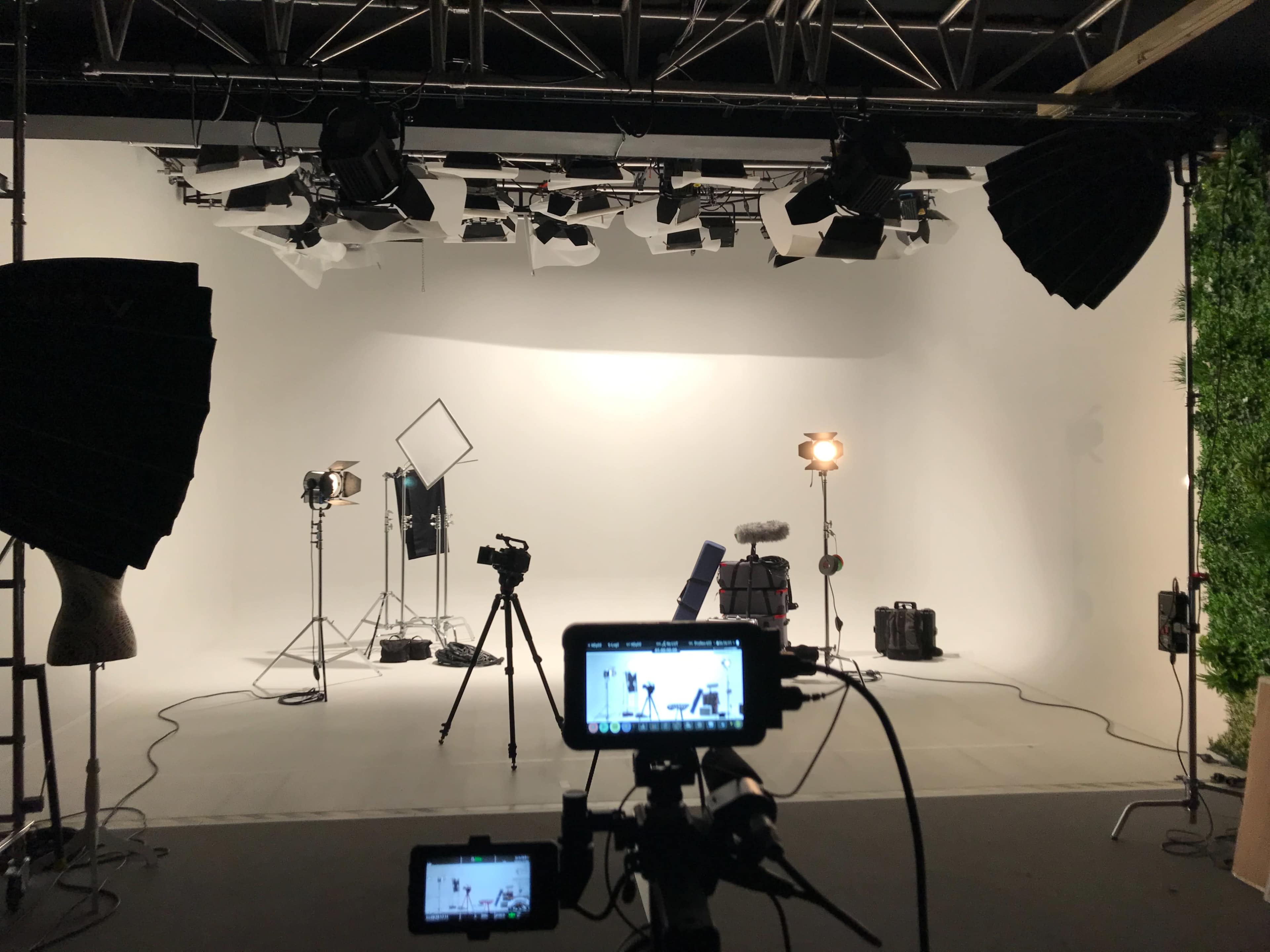 The image shows a well-equipped photography studio with various lights, cameras, and equipment set up against a white backdrop.