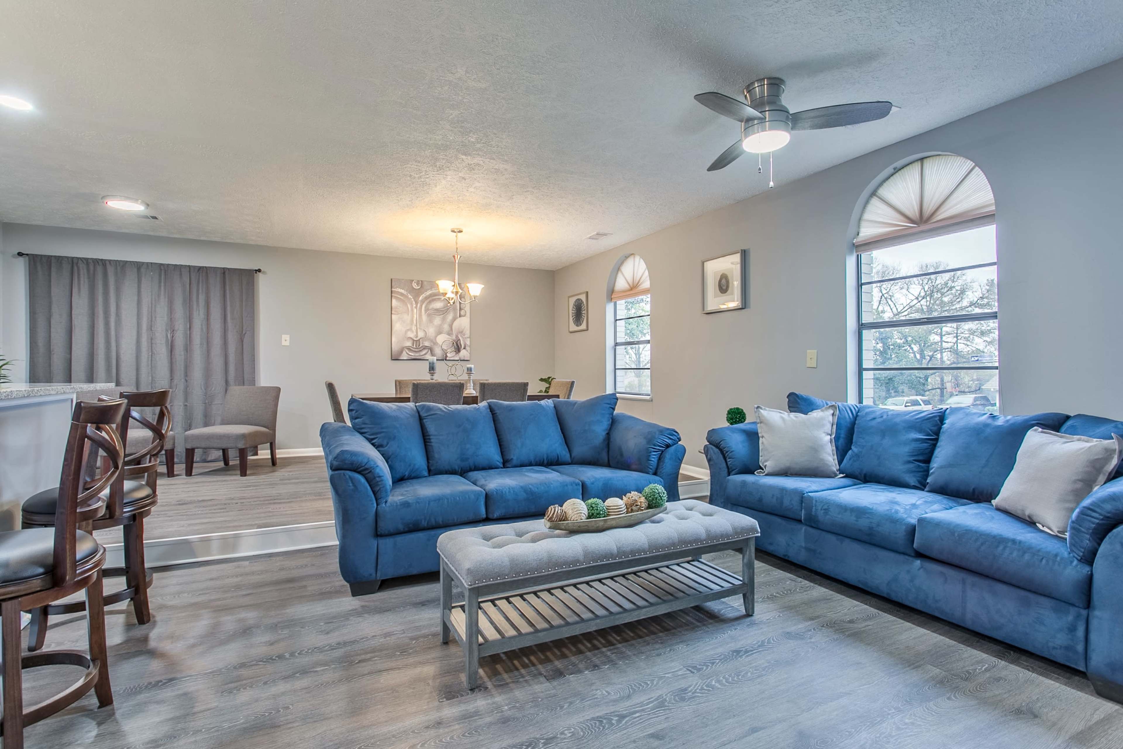 A modern living room with blue sofas, a coffee table, and large windows letting in natural light.