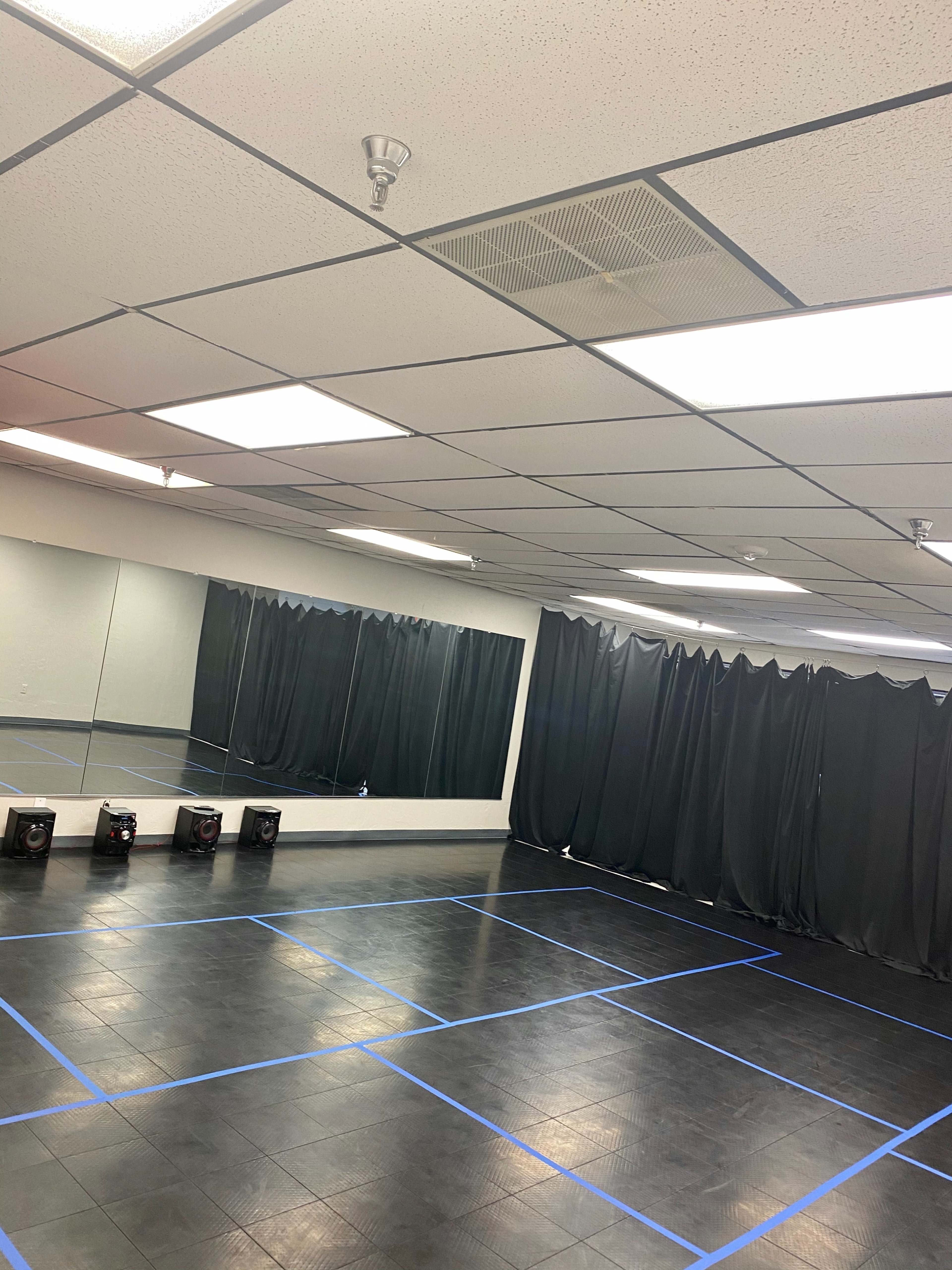 A spacious dance studio with wooden flooring, mirrored walls, and black curtains arranged along one side.