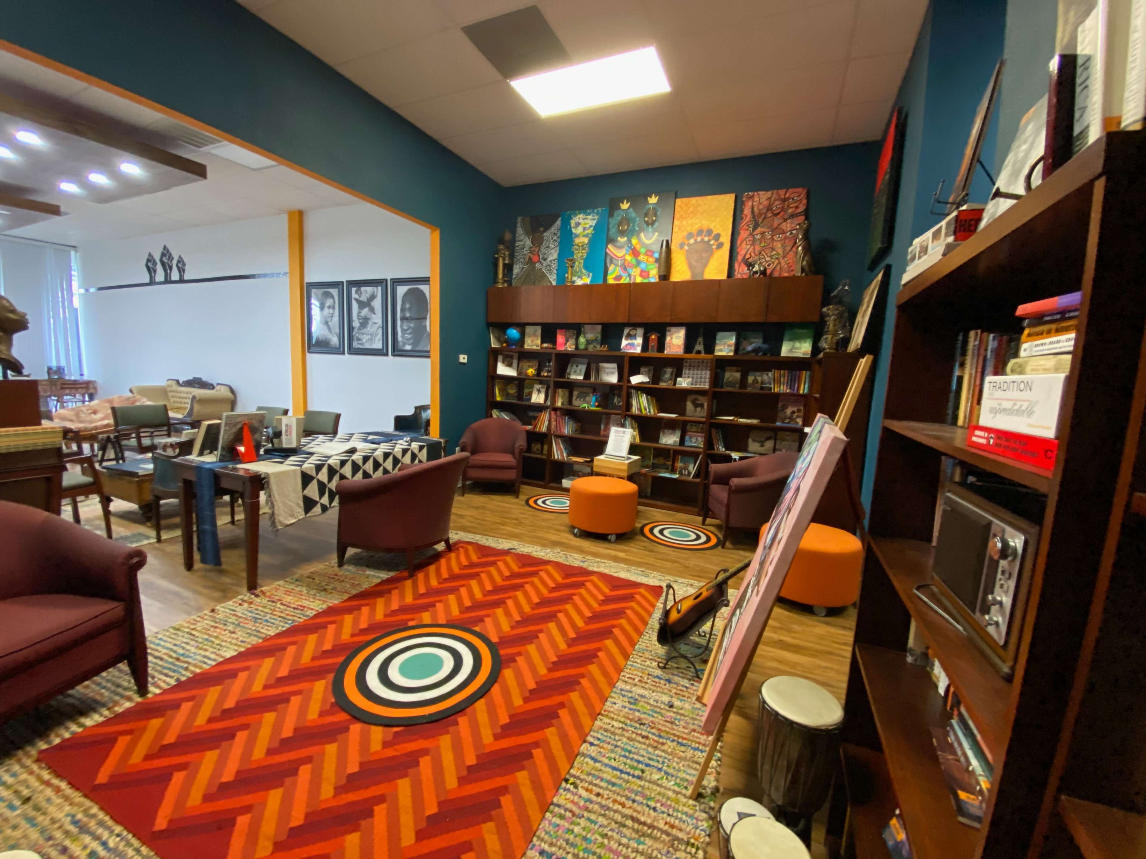 A cozy room with colorful art on the walls, bookshelves filled with books, and comfortable seating arranged around a patterned rug.