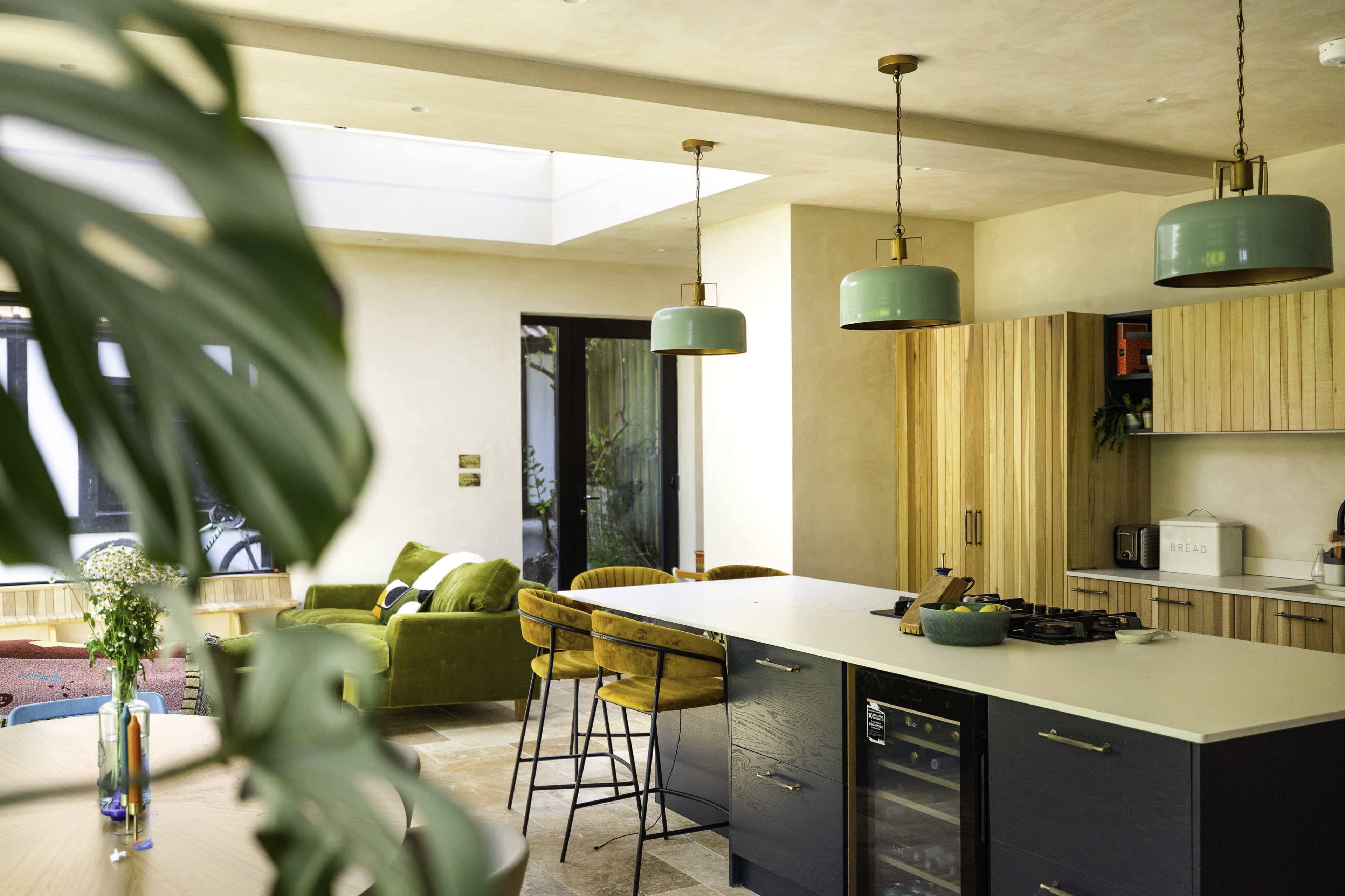 A modern kitchen with wooden cabinetry, green pendant lights, and a central island featuring bar stools.