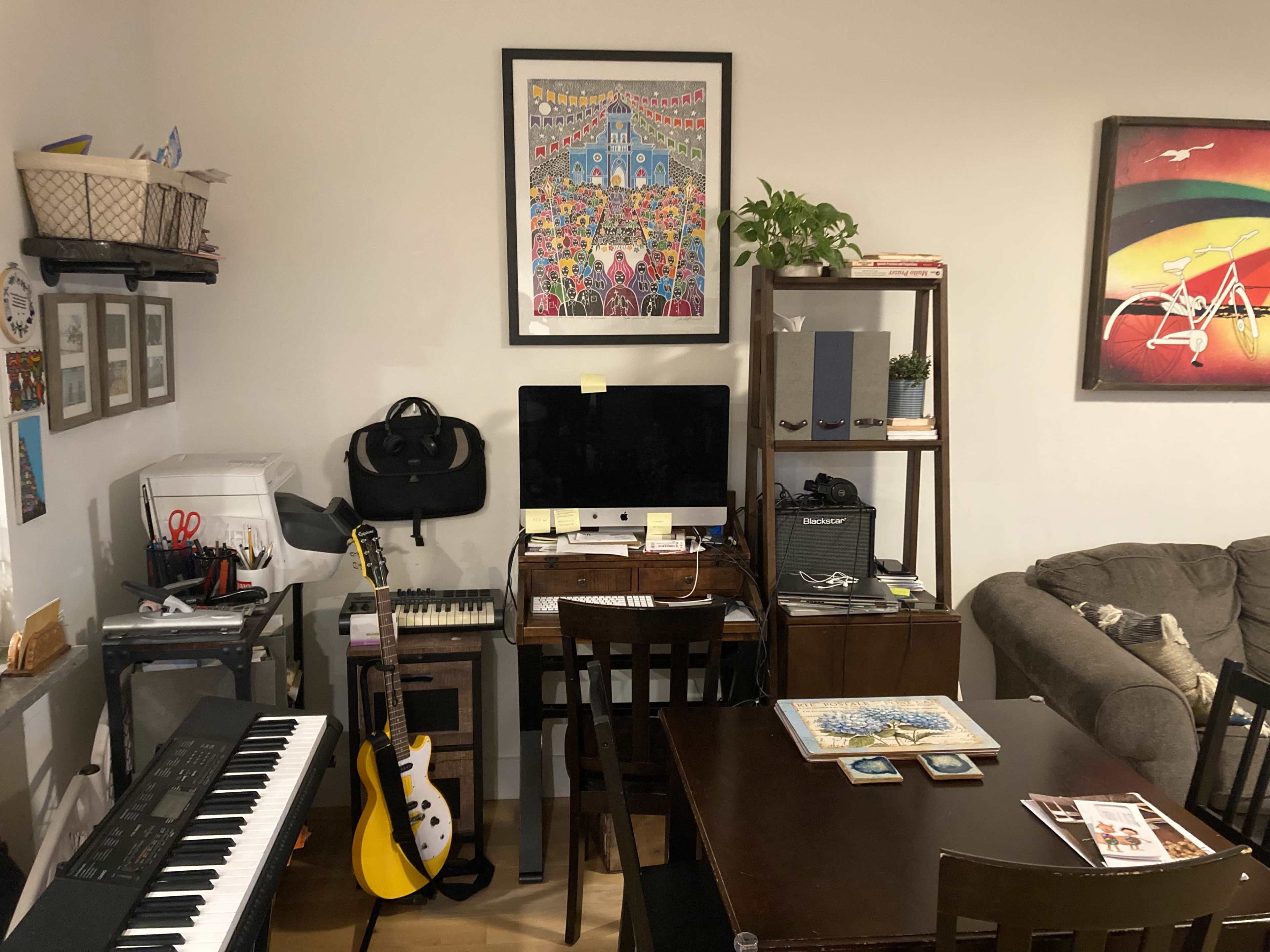 A home office setup is visible, featuring a computer on a desk, a keyboard, shelves with various items, and a sofa in the background.