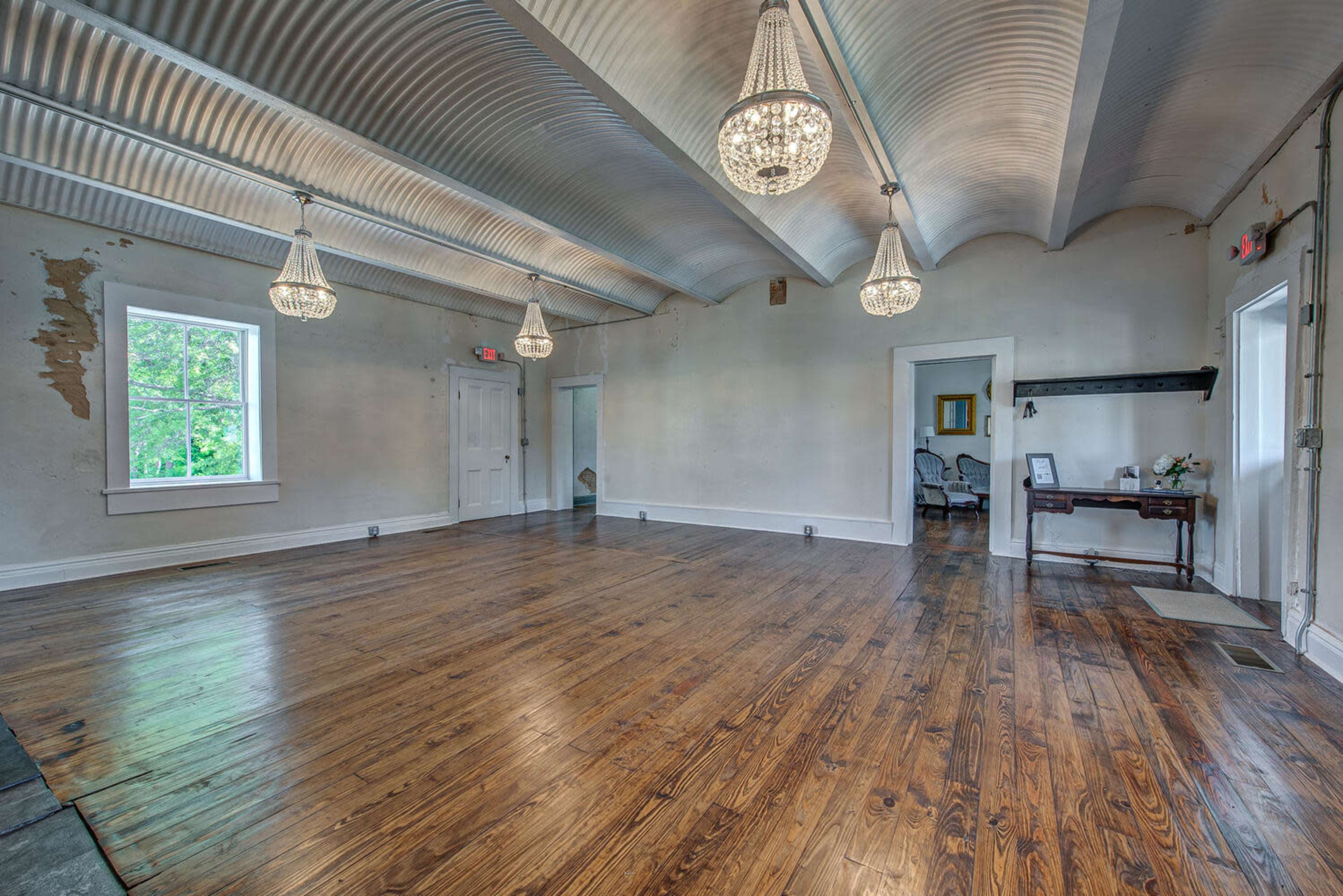 The image shows a spacious room with wooden flooring, high ceilings, and several hanging light fixtures.