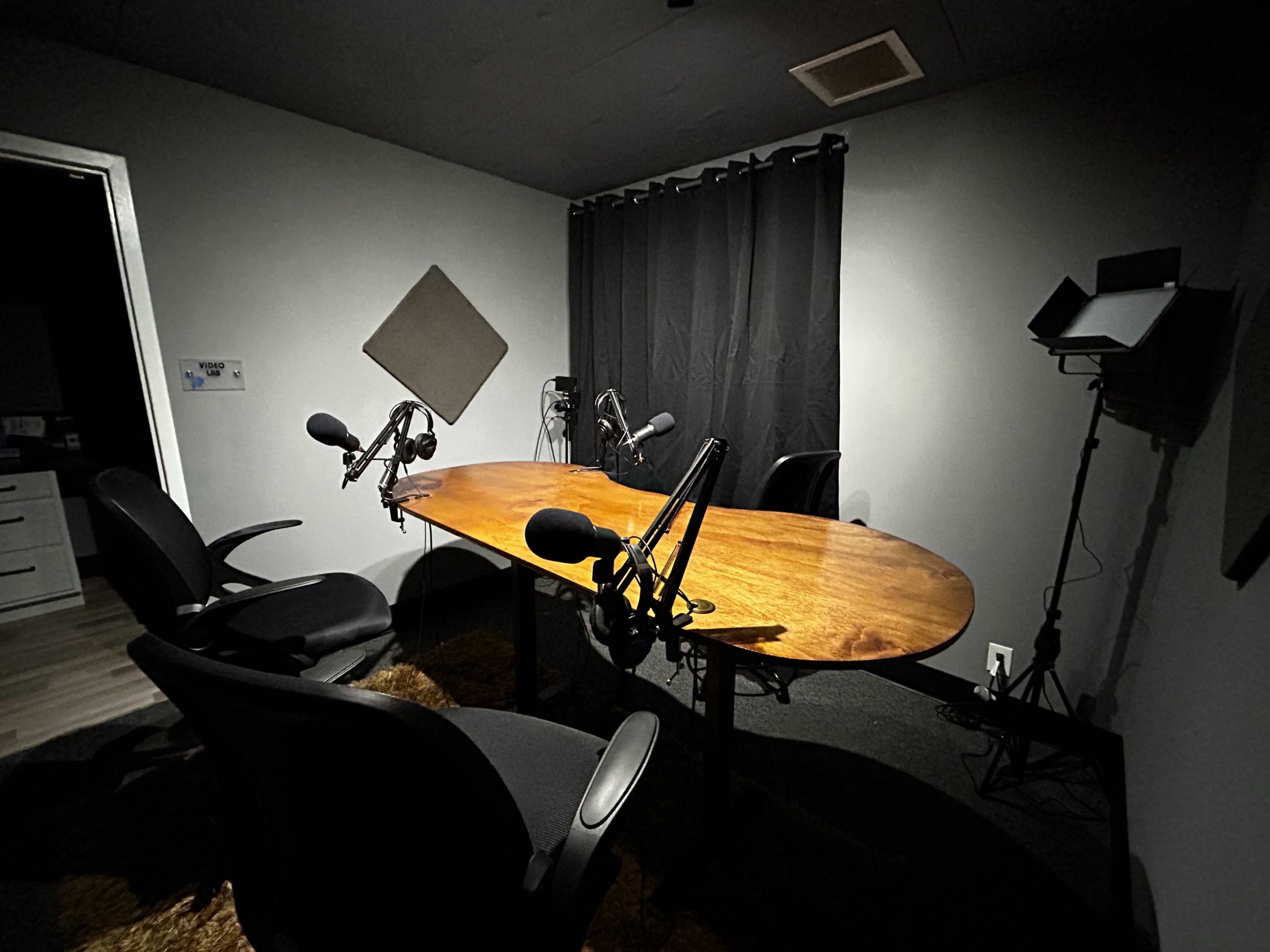 A small recording studio with a large oval table, two chairs, and multiple microphones set up around the table.